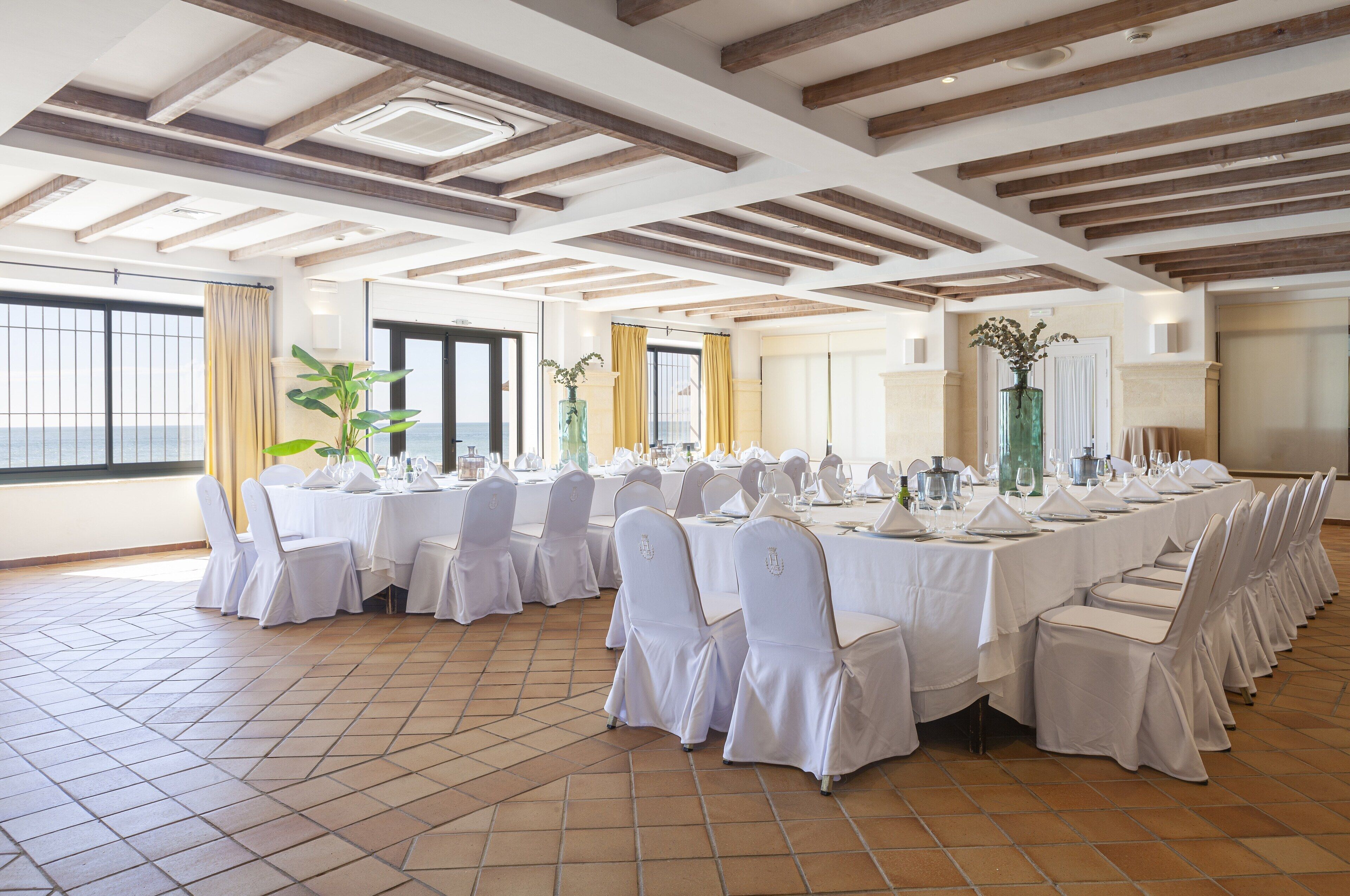 Un salón de banquetes con manteles blancos, sillas y suelo de baldosas.