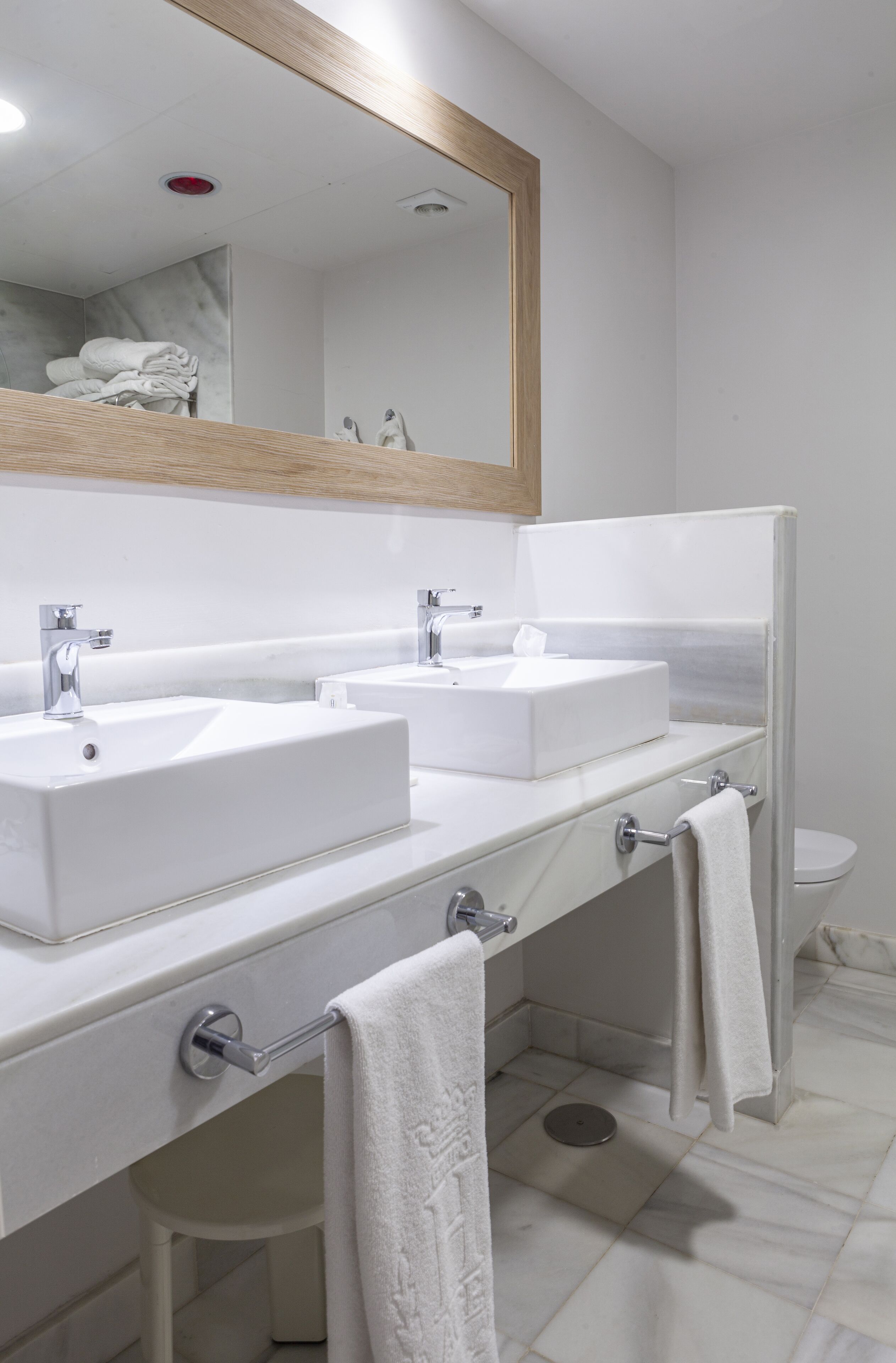 A modern bathroom with two sinks, a mirror, and a toilet.