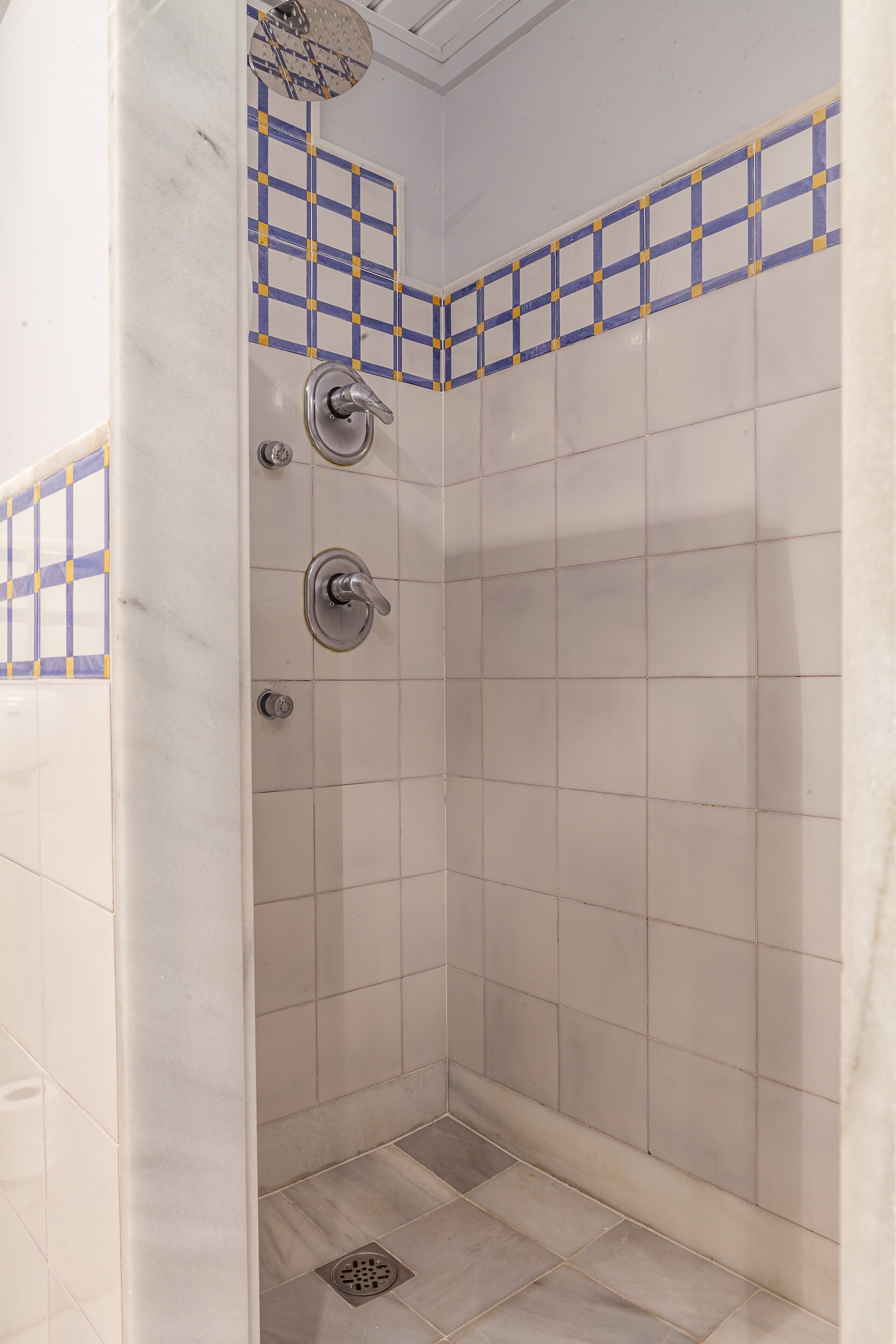Um chuveiro pequeno revestido com azulejos, com ralo e chuveiro.