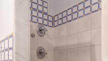 Um chuveiro pequeno revestido com azulejos, com ralo e chuveiro.