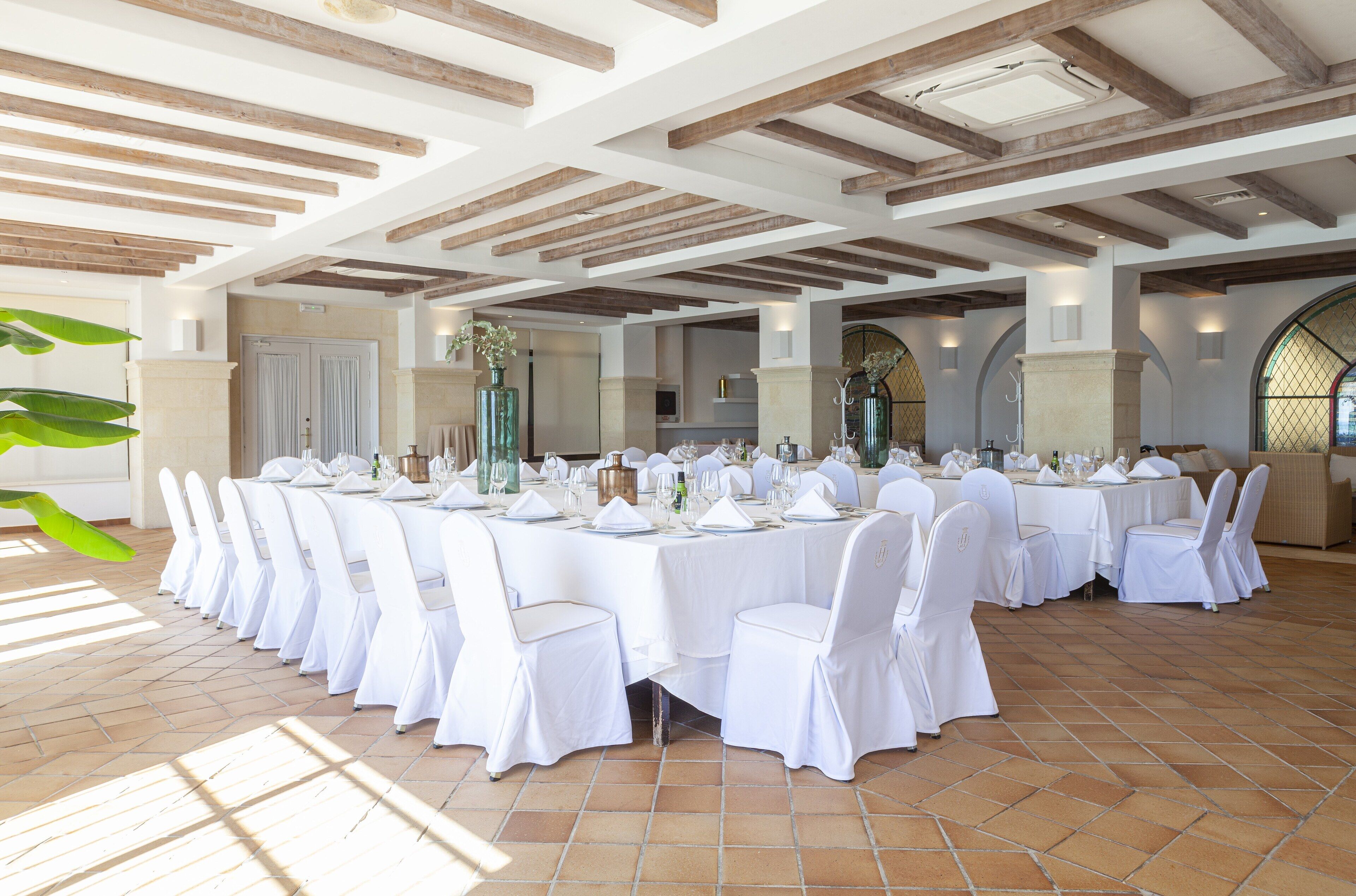 Une salle de banquet avec des nappes blanches, des tables rondes et des chaises blanches.