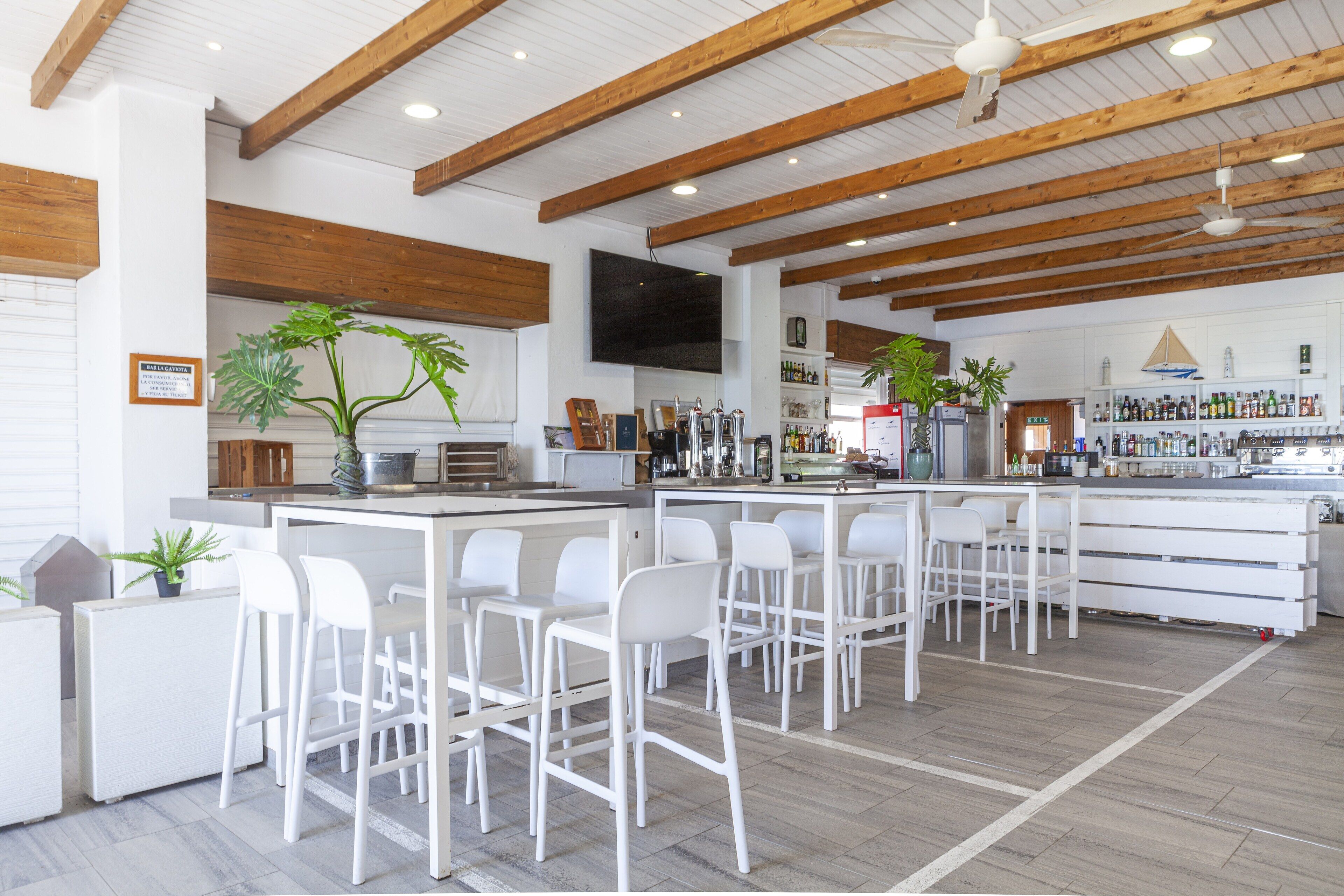 Eine moderne Bar mit weißen Barhocker, Holzbalken und verschiedenen Bartresuren.