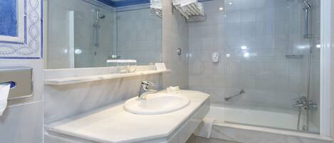Un baño moderno con un lavamanos blanco, una ducha con cerramiento de vidrio y un espejo grande.