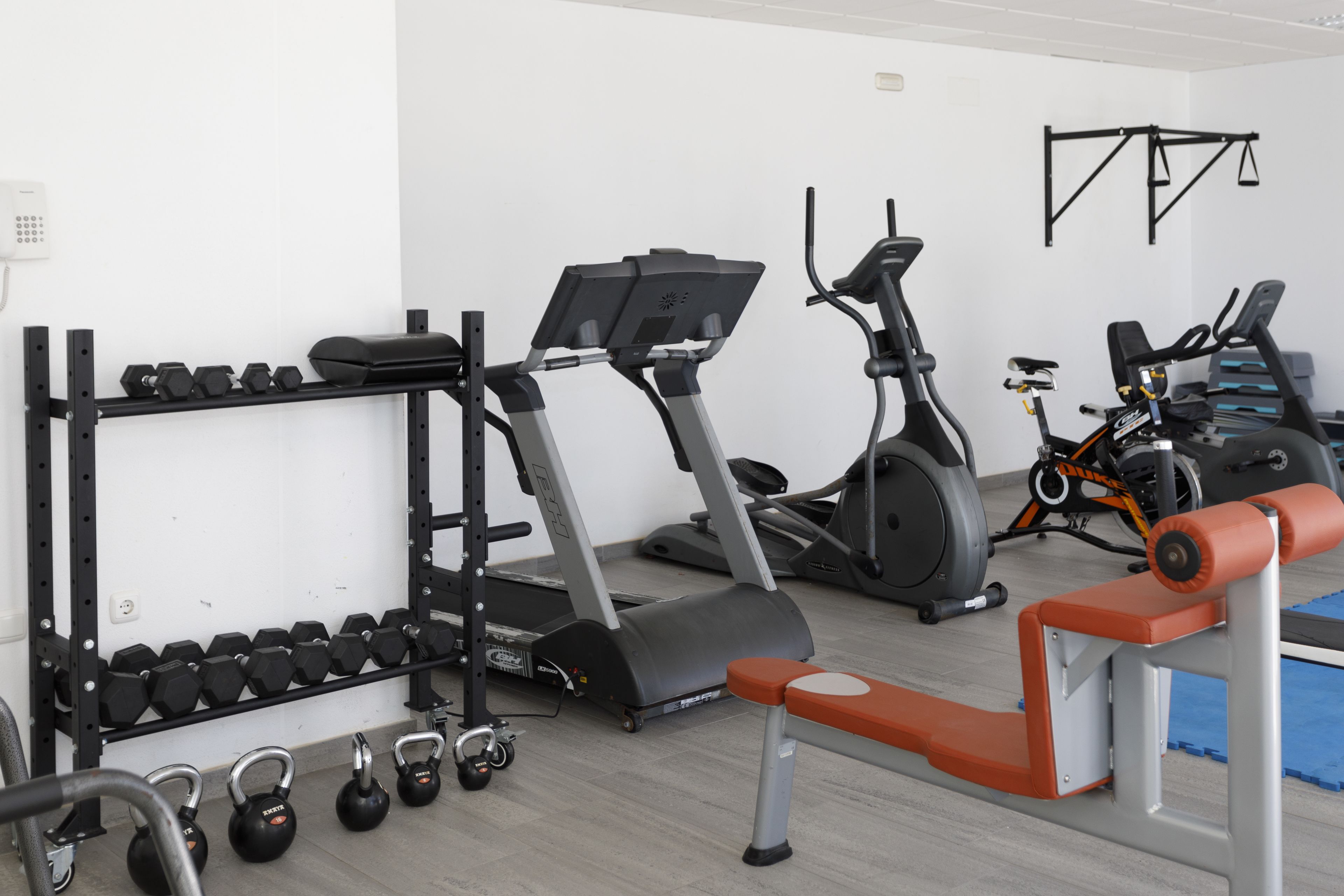A gym with exercise equipment including treadmills, a bench, and dumbbells.
