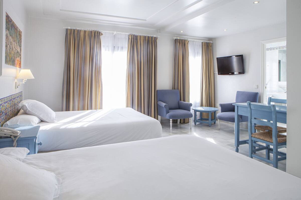 Une chambre d’hôtel avec deux lits, un bureau, une chaise, une télévision et une lampe.