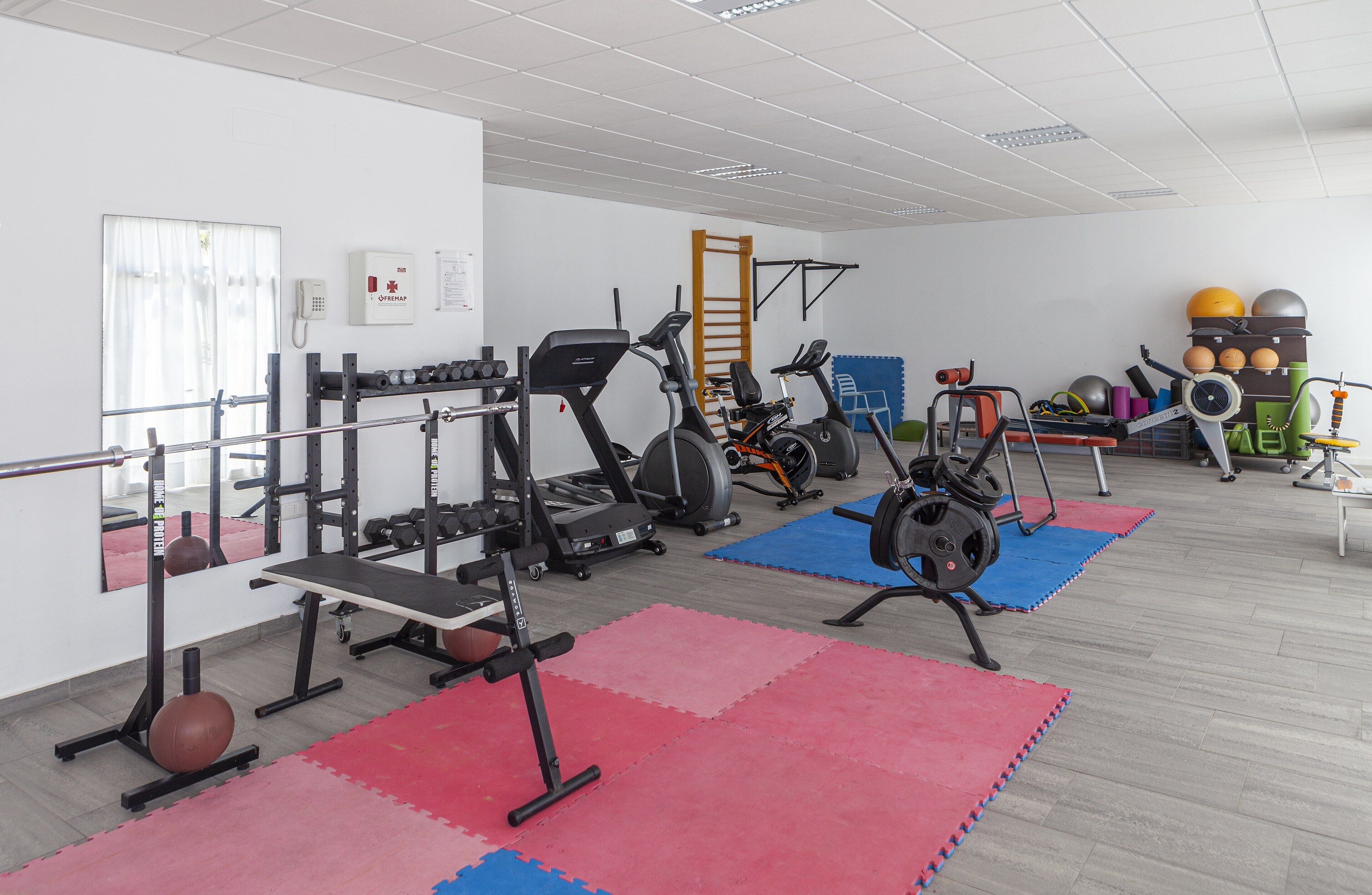 A gym with exercise equipment, mats, and a phone on the wall.