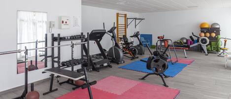 A gym with exercise equipment, mats, and a phone on the wall.