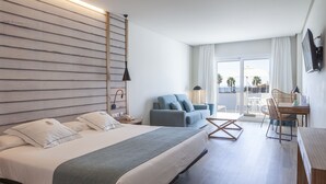 Habitación de hotel con una cama grande, un sofá, una mesa de comedor y un balcón con vistas.