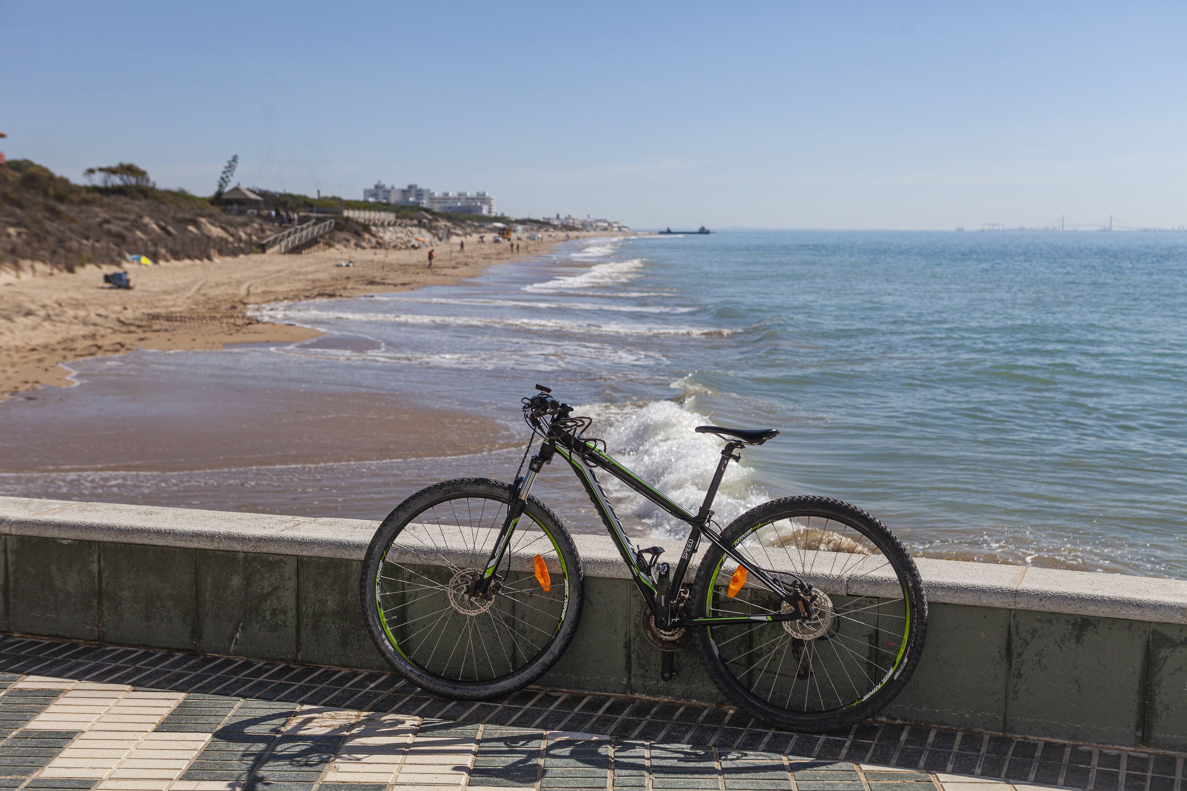 Una bicicletta appoggiata a una barriera di cemento vicino a una spiaggia, con le onde che si infrangono sulla riva.