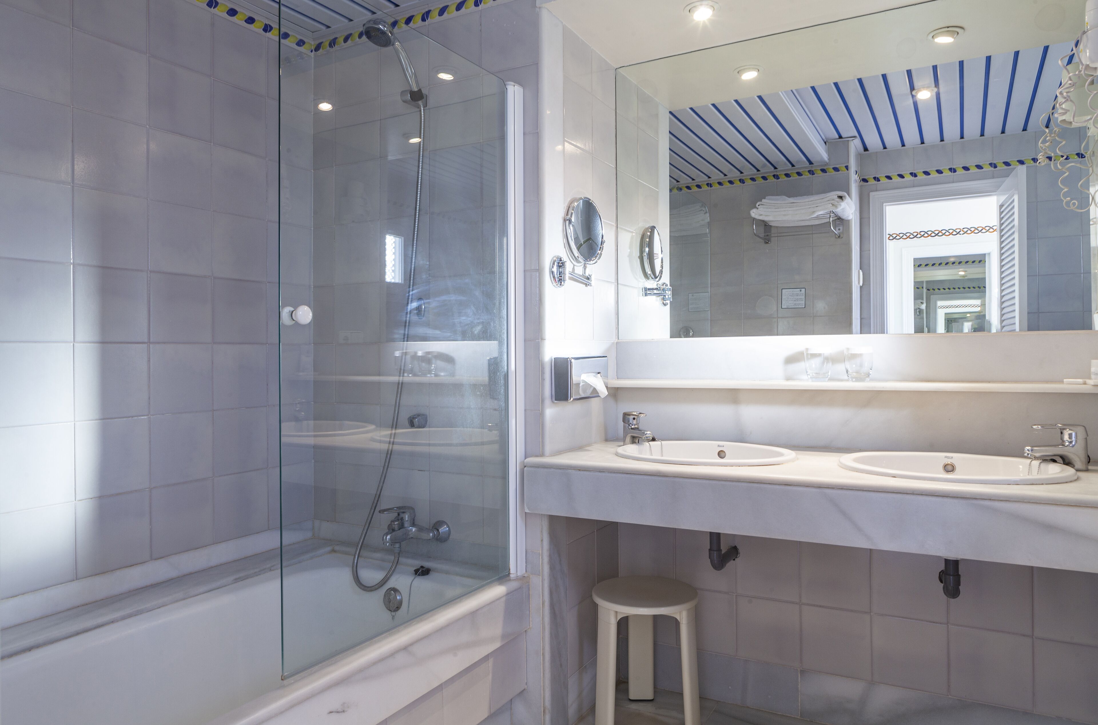 Une salle de bain moderne dotée d’une douche à parois de verre, de deux lavabos et d’un grand miroir.