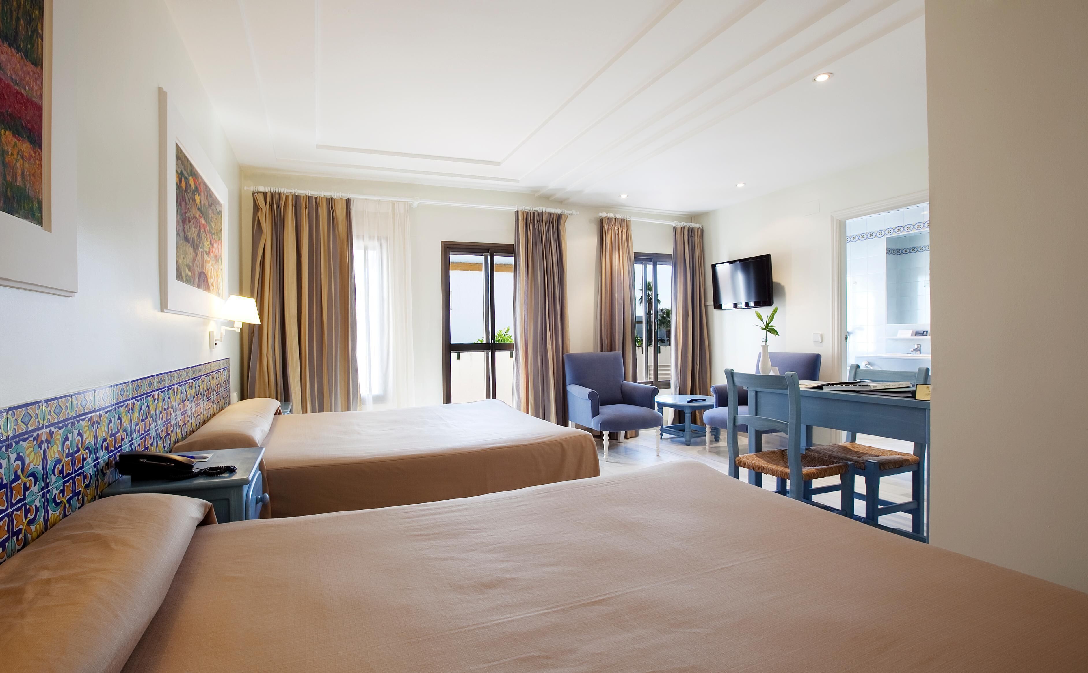 Une chambre d’hôtel avec deux lits, un bureau avec une chaise, une télévision et une fenêtre avec des rideaux.
