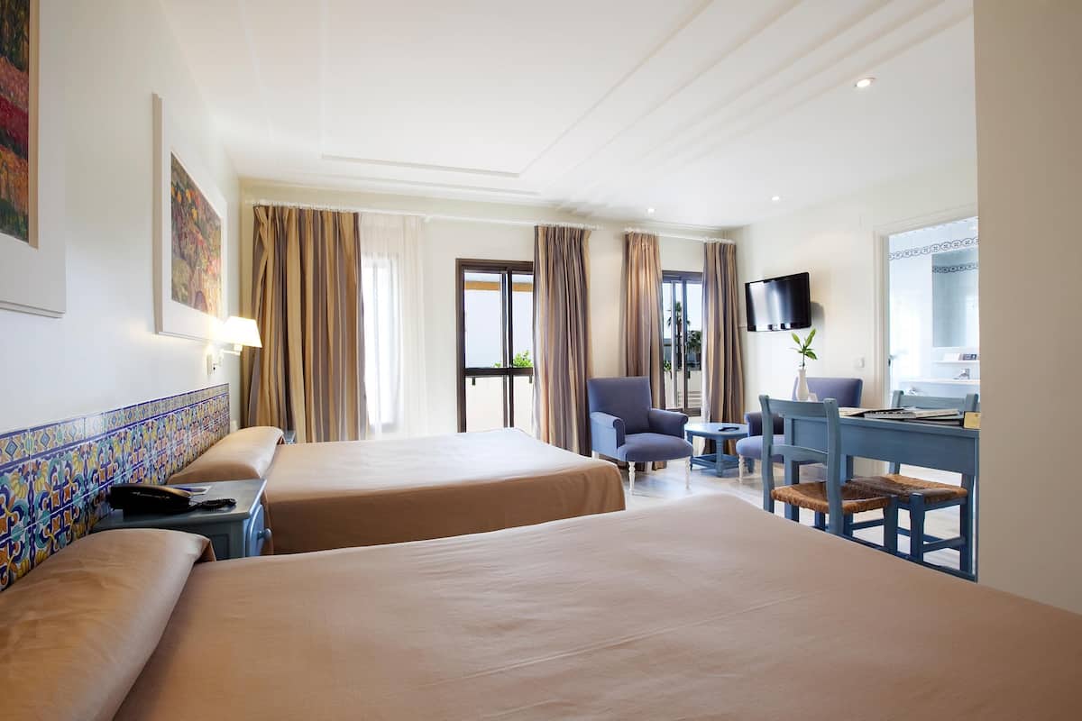 Ein Hotelzimmer mit zwei Betten, einem Schreibtisch mit Stuhl, einem Fernseher und einem Fenster mit Vorhängen.