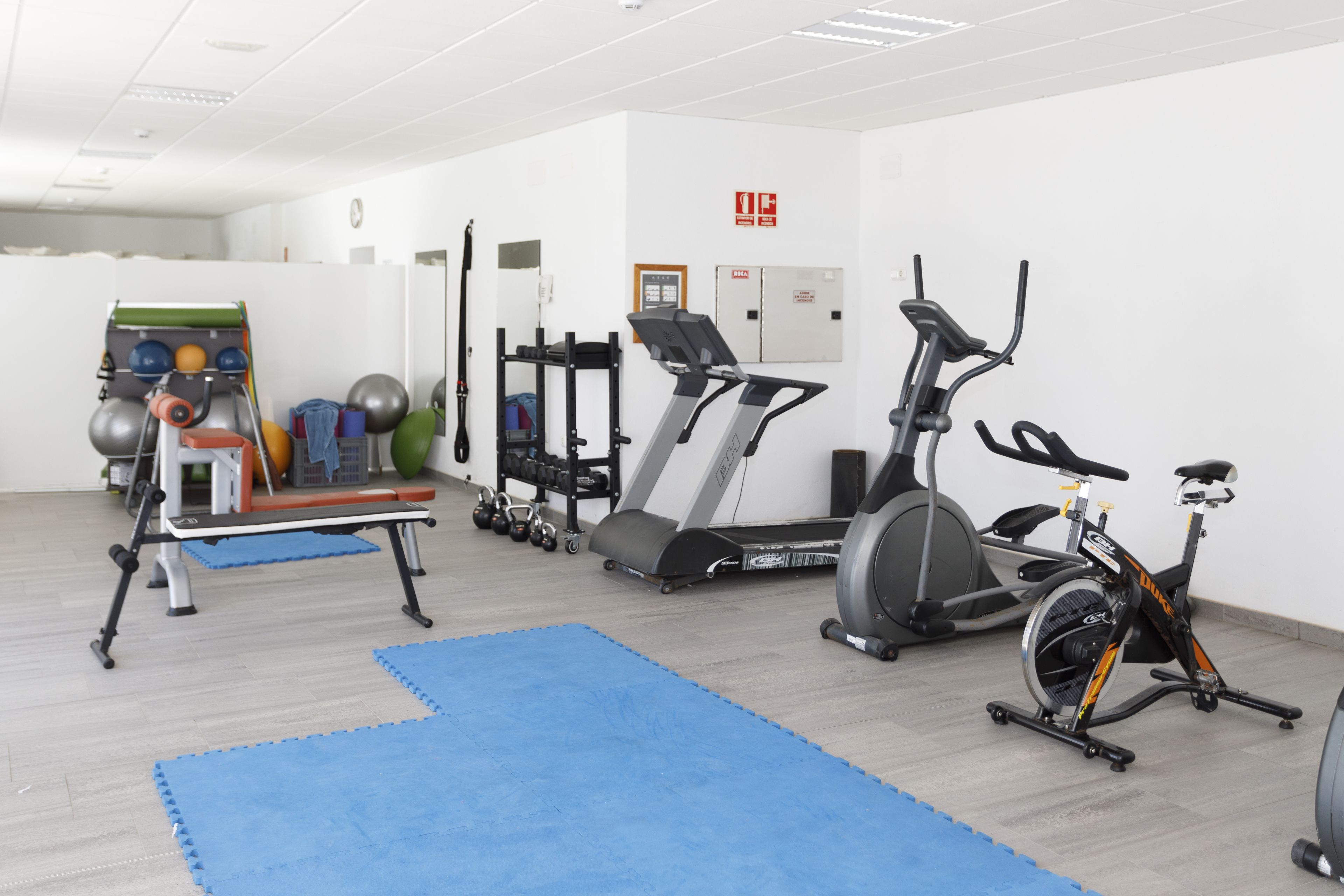 Gimnasio con equipo de ejercicio, incluyendo cinta de correr, bicicleta estática y pesas.