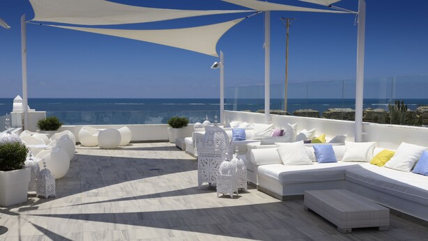 Una terraza en la azotea con mobiliario blanco, barandilla blanca y vista al mar.