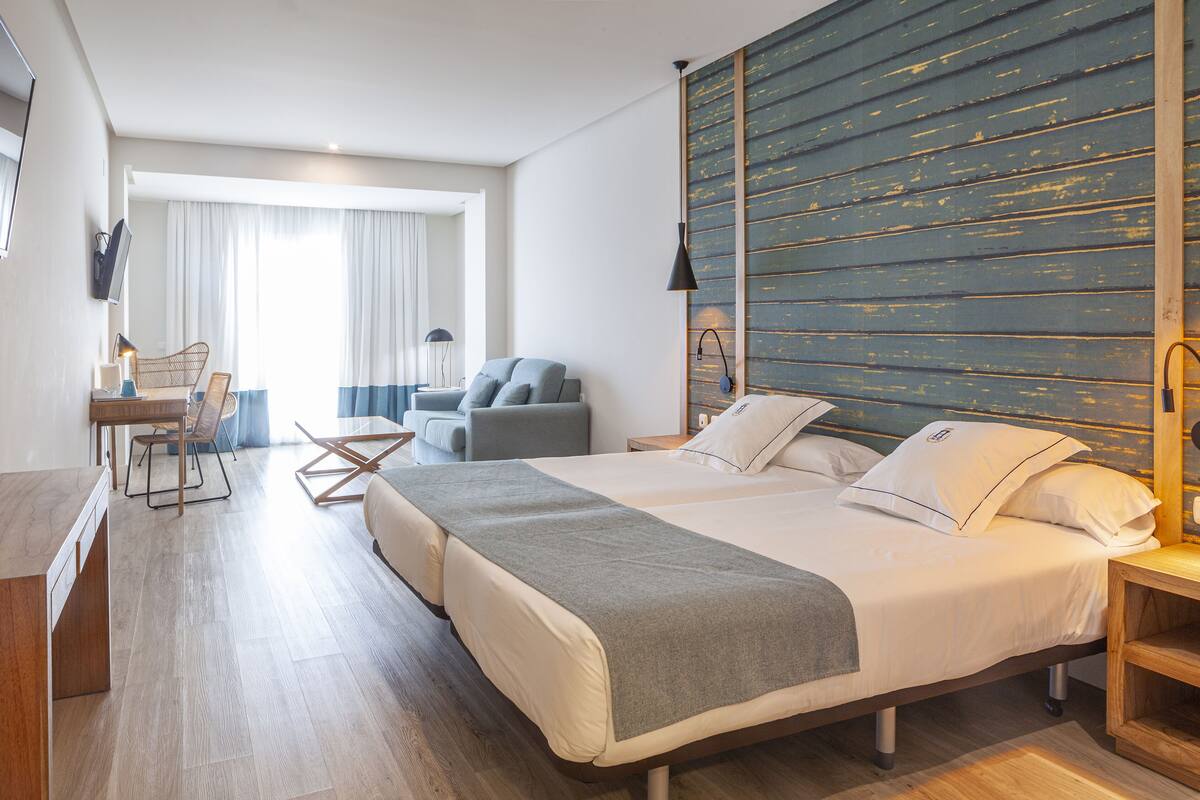 Une chambre d’hôtel moderne dotée d’un grand lit, d’un bureau avec une chaise, d’un canapé et offrant une vue sur l’extérieur grâce à une grande fenêtre.