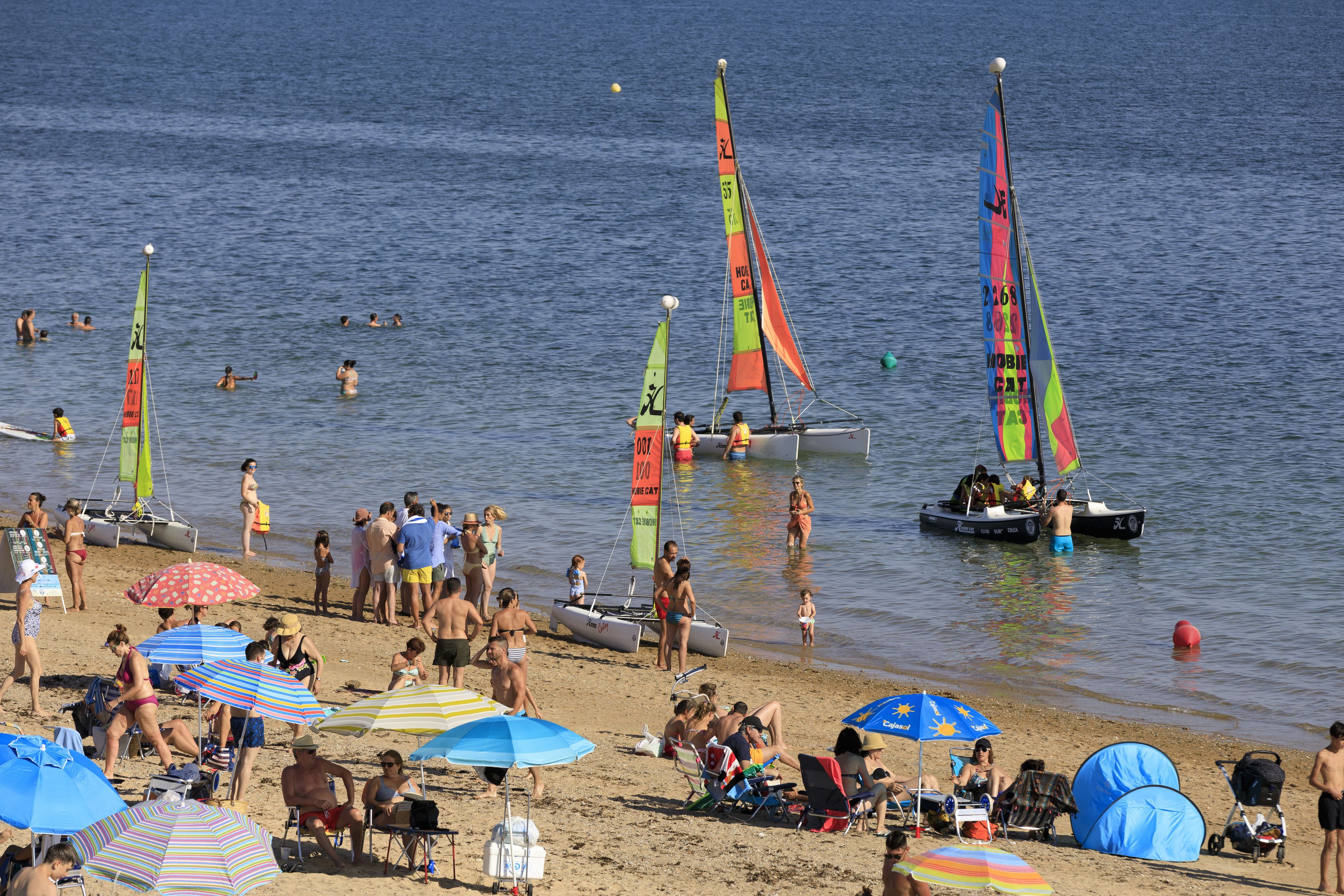 Une plage avec des gens, des bateaux et des parasols.