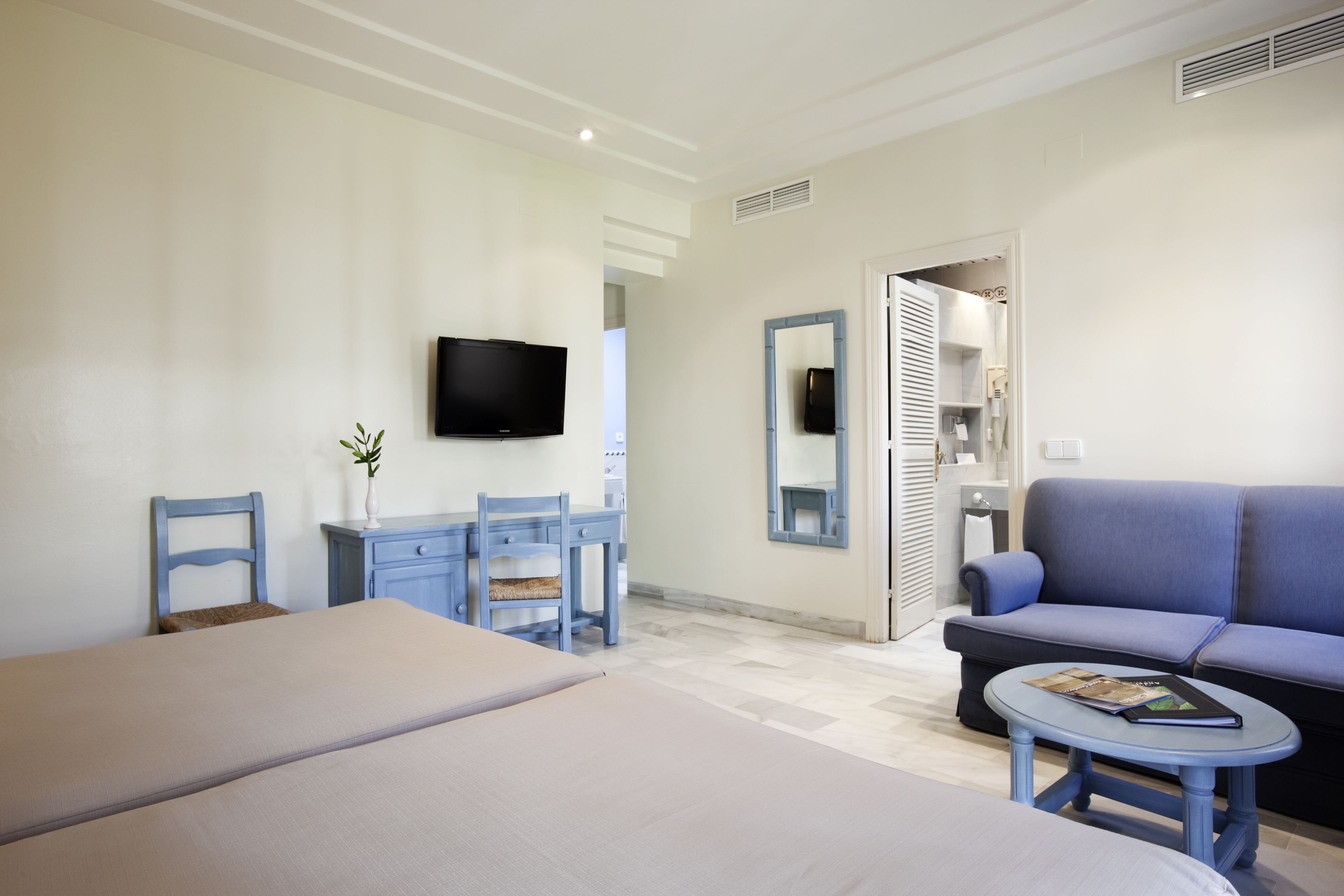 A hotel room with a bed, a desk with a chair, a sofa, a small table, a television, and a mirror.