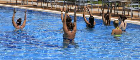 A swimming pool with people raising their hands, surrounded by lounge chairs and tables.