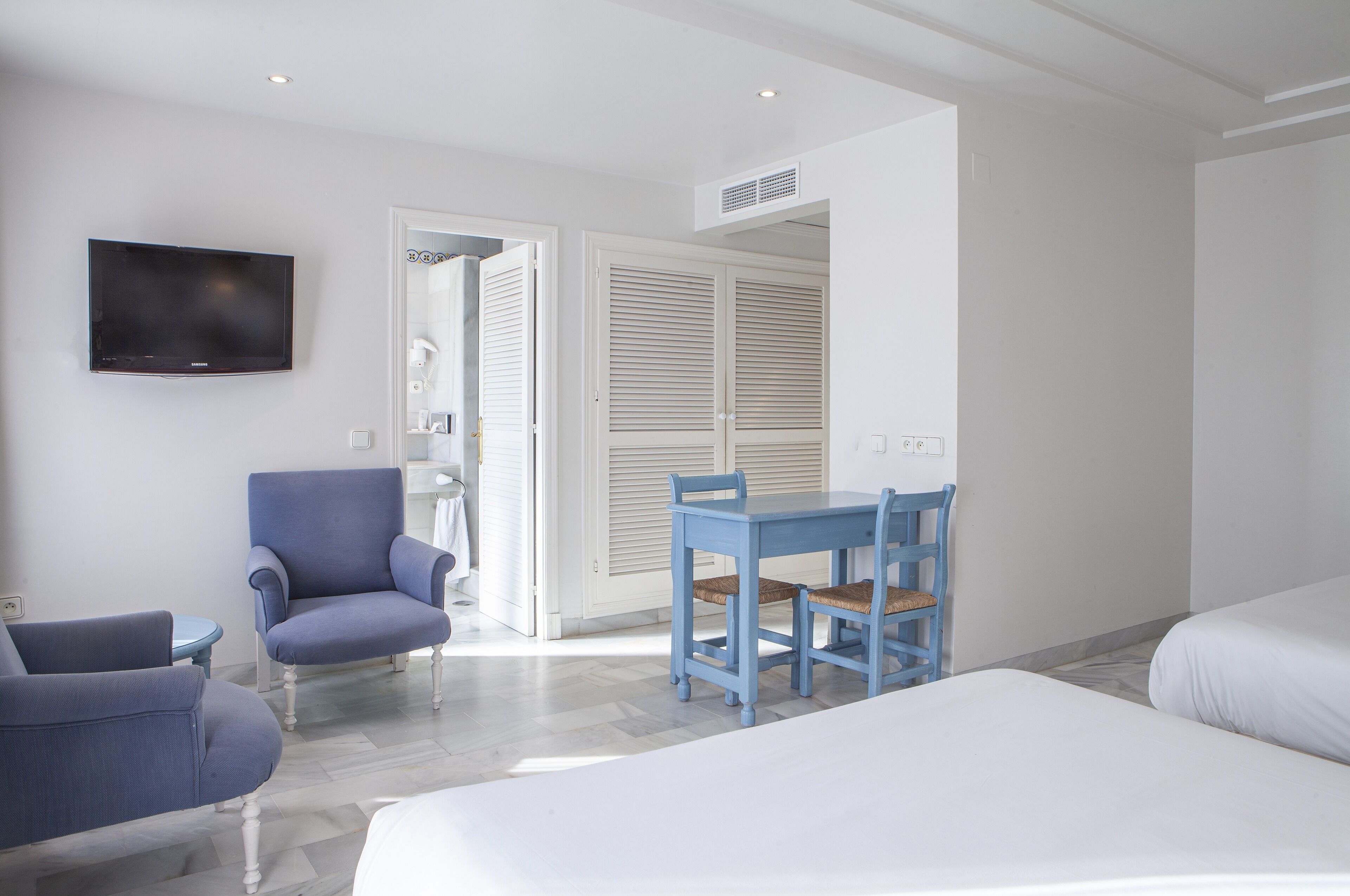 A hotel room with a bed, a desk with chairs, a TV, and a wardrobe.