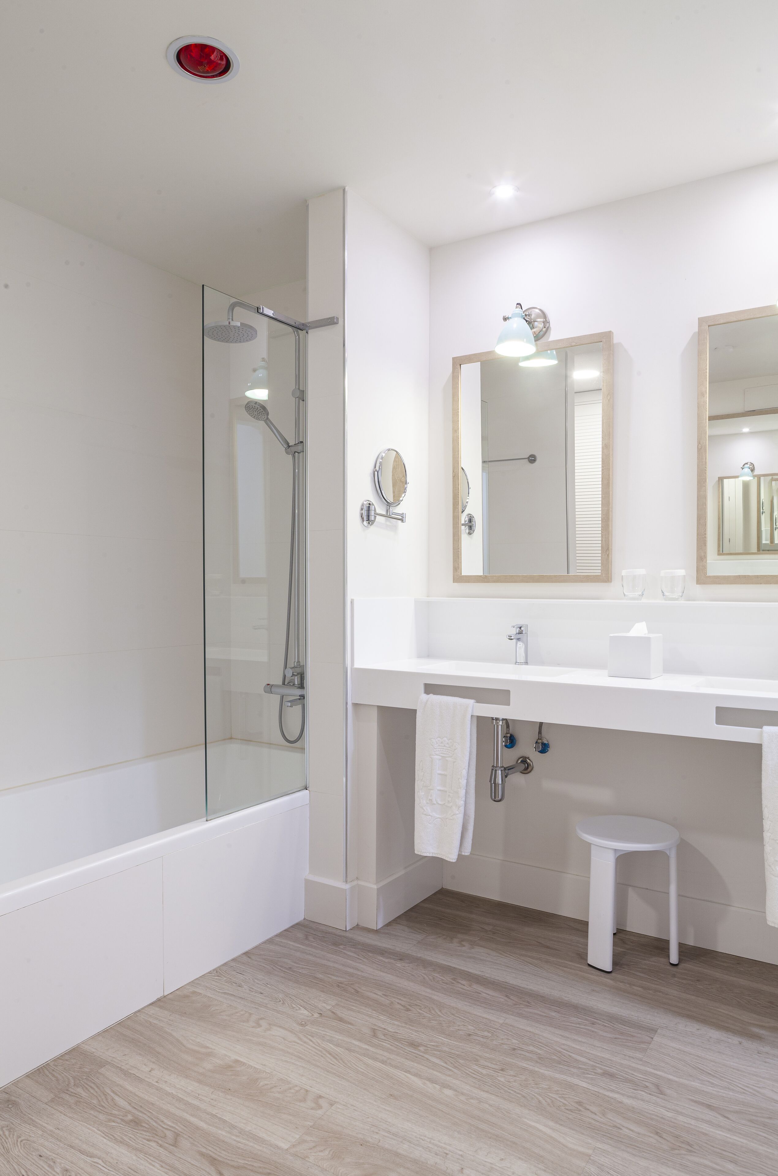 Un baño moderno con ducha de vidrio, un lavamanos blanco con espejo y suelo de madera.