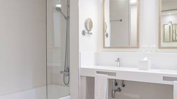 Un baño moderno con ducha de vidrio, un lavamanos blanco con espejo y suelo de madera.