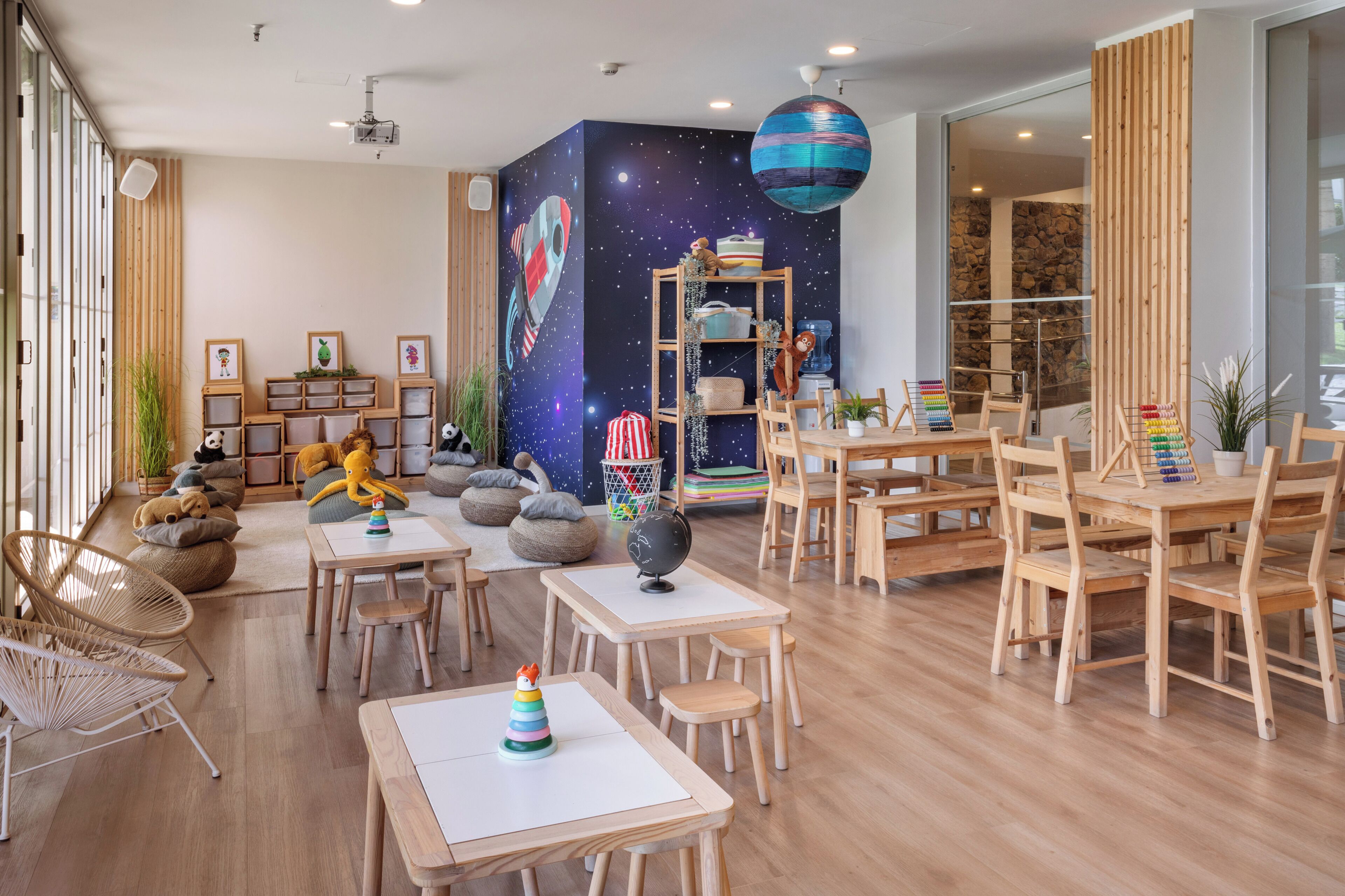 Ruime kamer met houten meubels, een boekenplank, een wereldbol en een muurschildering van een sterrenhemel.