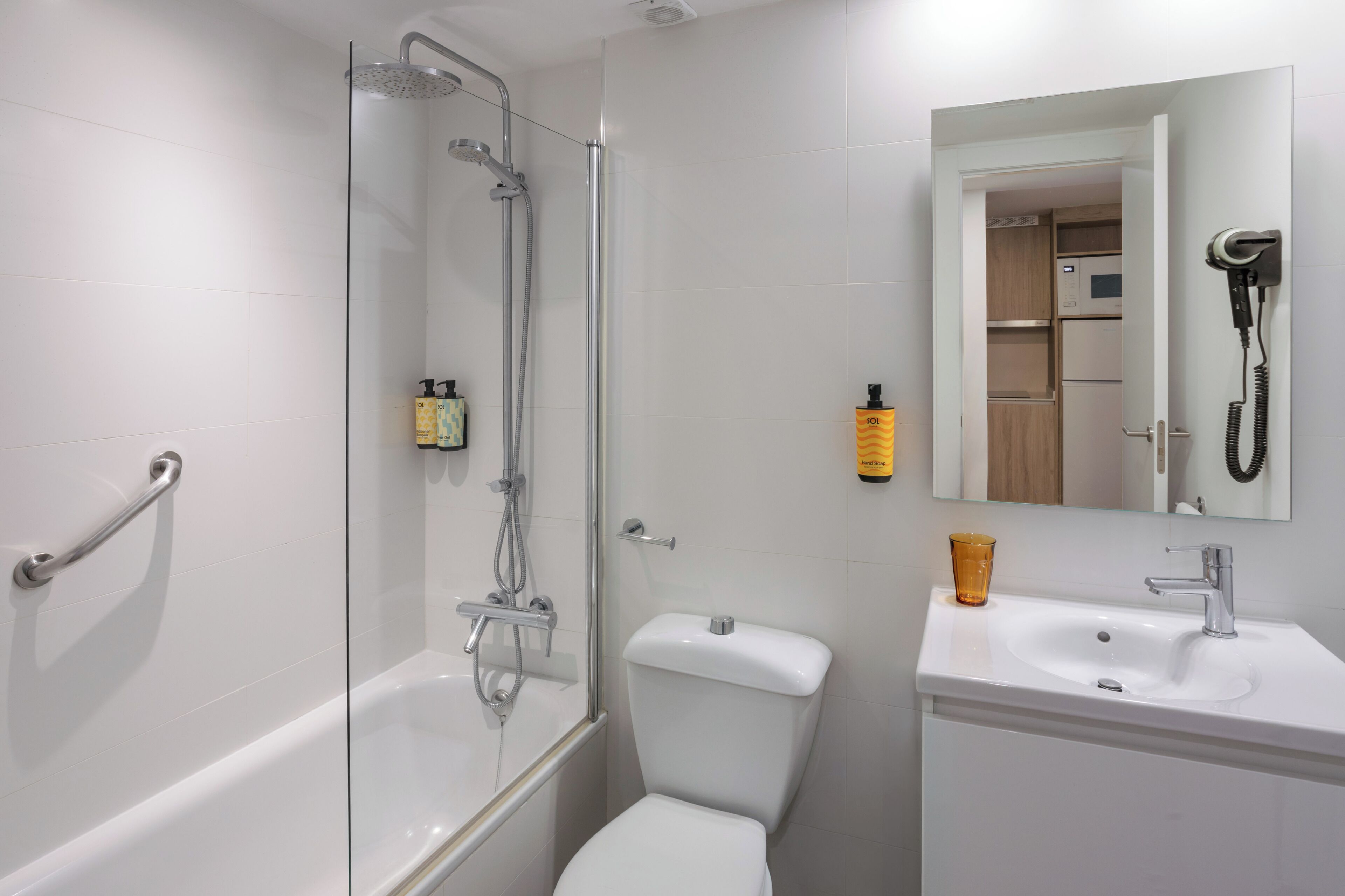 A bathroom with a glass-enclosed shower, a toilet, a sink, and a mirror with a hairdryer mounted on the wall.