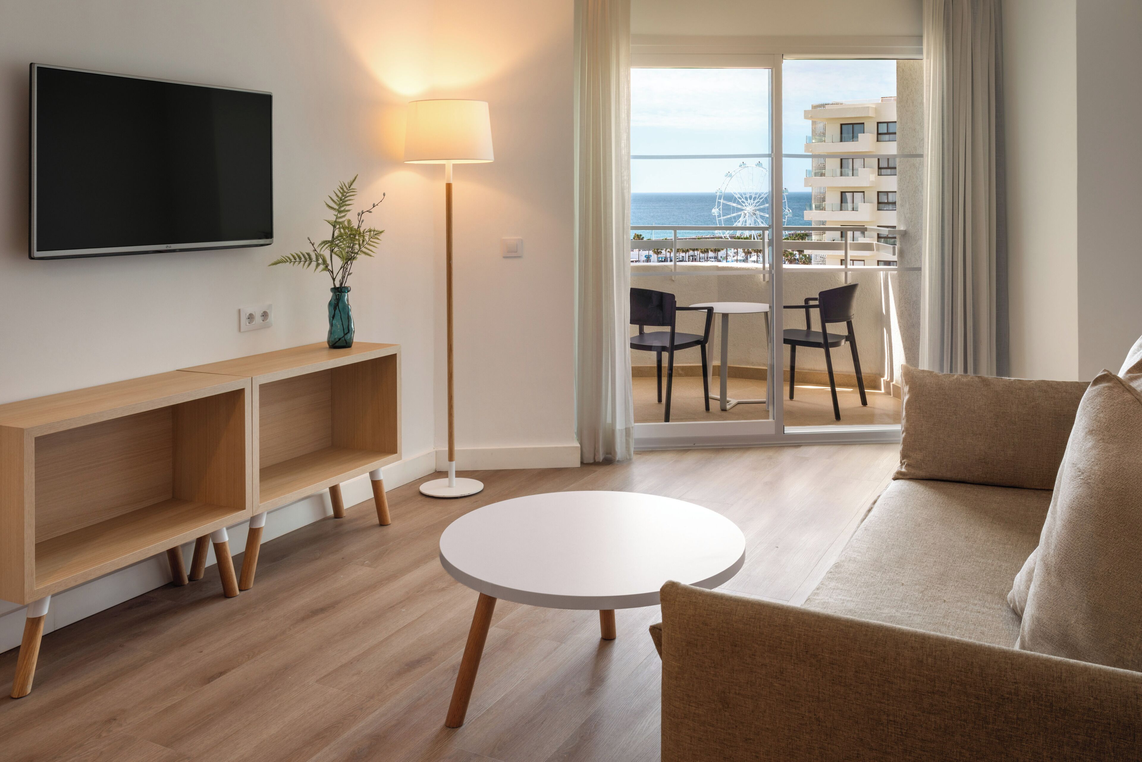 Un salon moderne doté d’un téléviseur à écran plat, d’une table ronde blanche, d’un canapé et offrant une vue sur un balcon avec une grande roue.