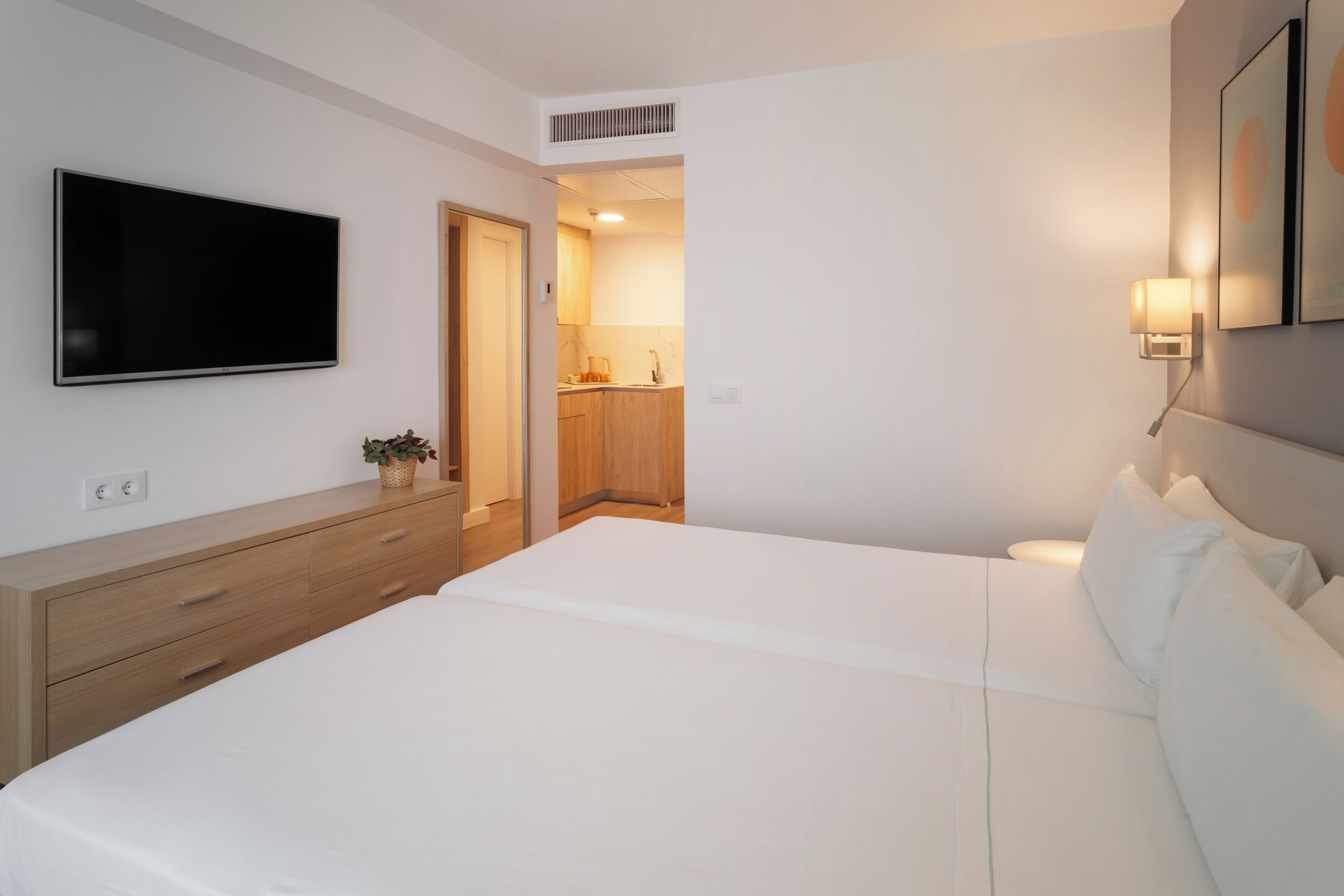 A bedroom with a large bed, a TV, a bedside table, and a wall-mounted light.