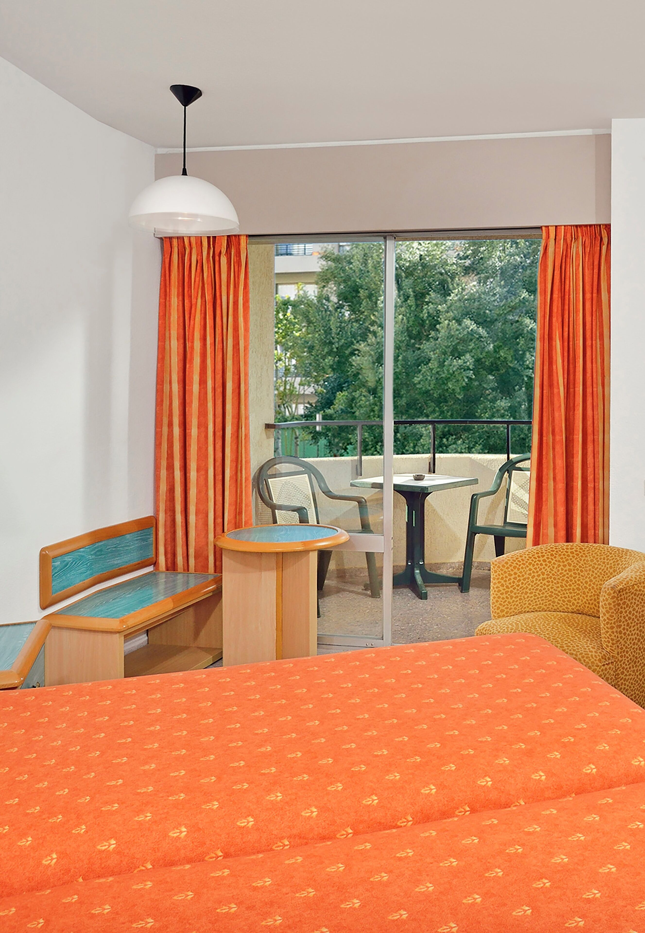 A hotel room with a bed, a small table, two chairs, and a balcony with a table and chairs.