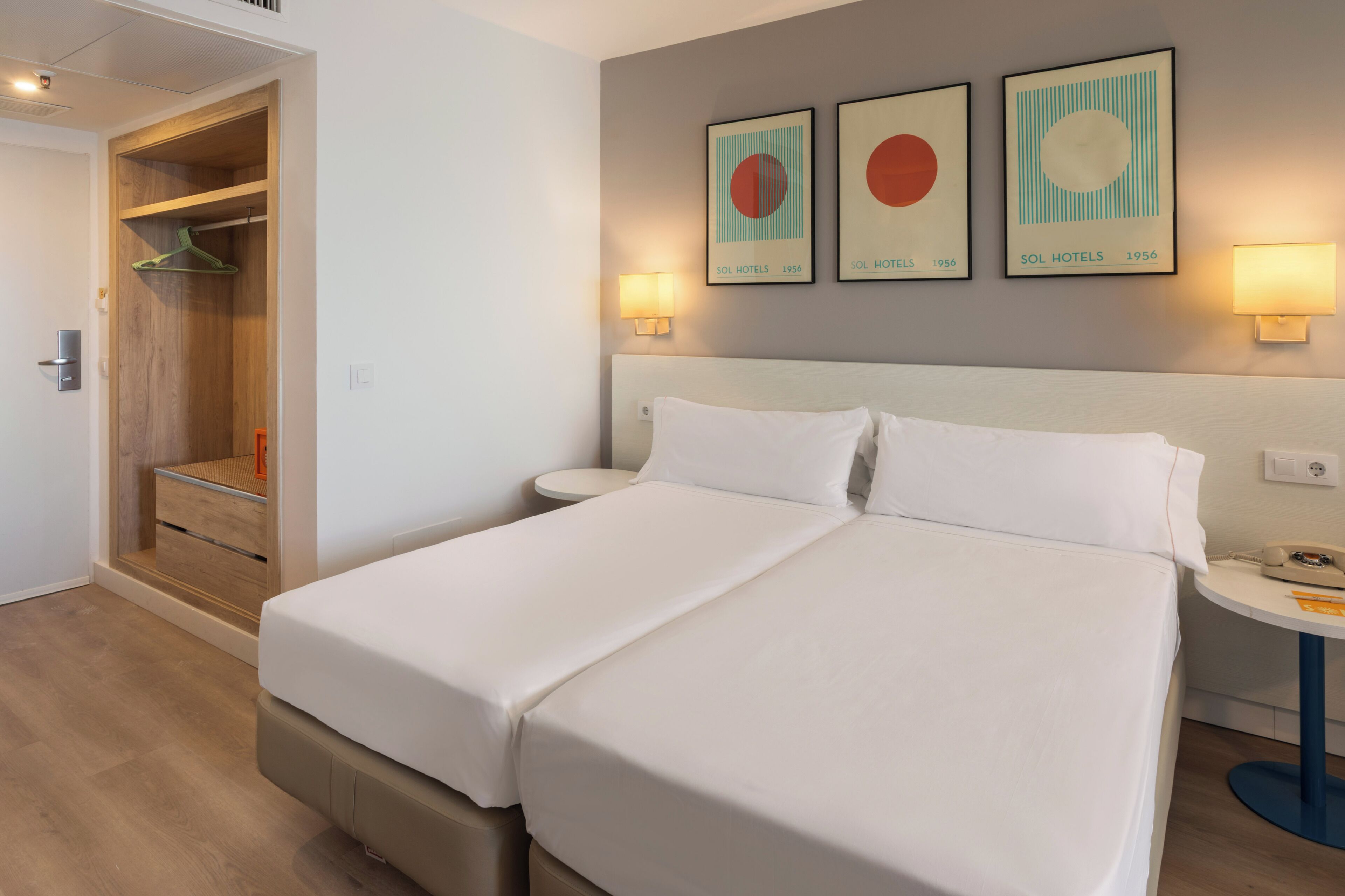 Une chambre d’hôtel avec un lit double, une table de chevet, une commode, une armoire et trois tableaux encadrés accrochés au mur.
