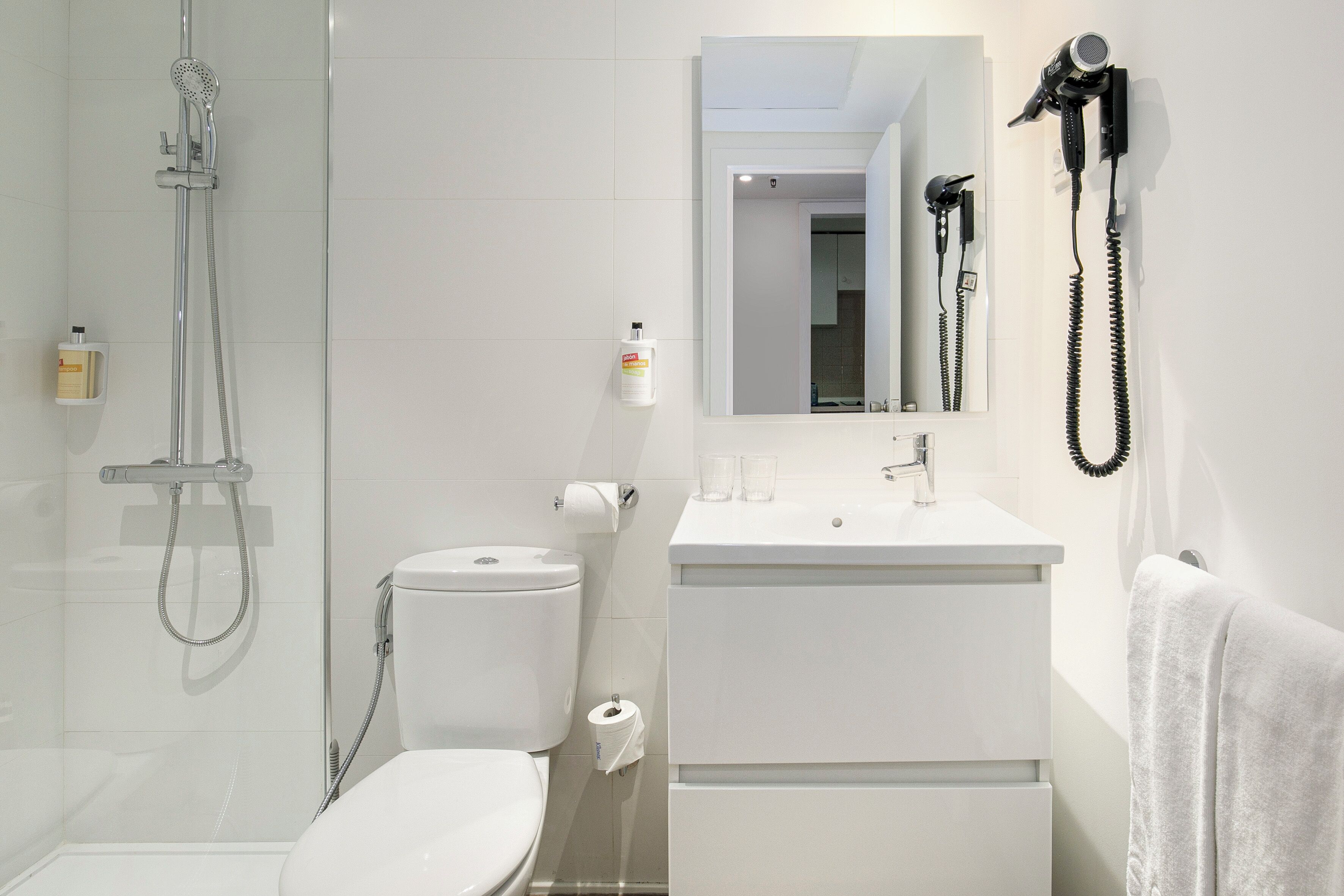 A modern bathroom with a toilet, shower, sink, and a hairdryer mounted on the wall.