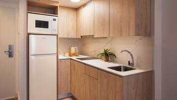 A compact kitchen with wooden cabinets, a built-in microwave, a stainless steel sink, and a potted plant.