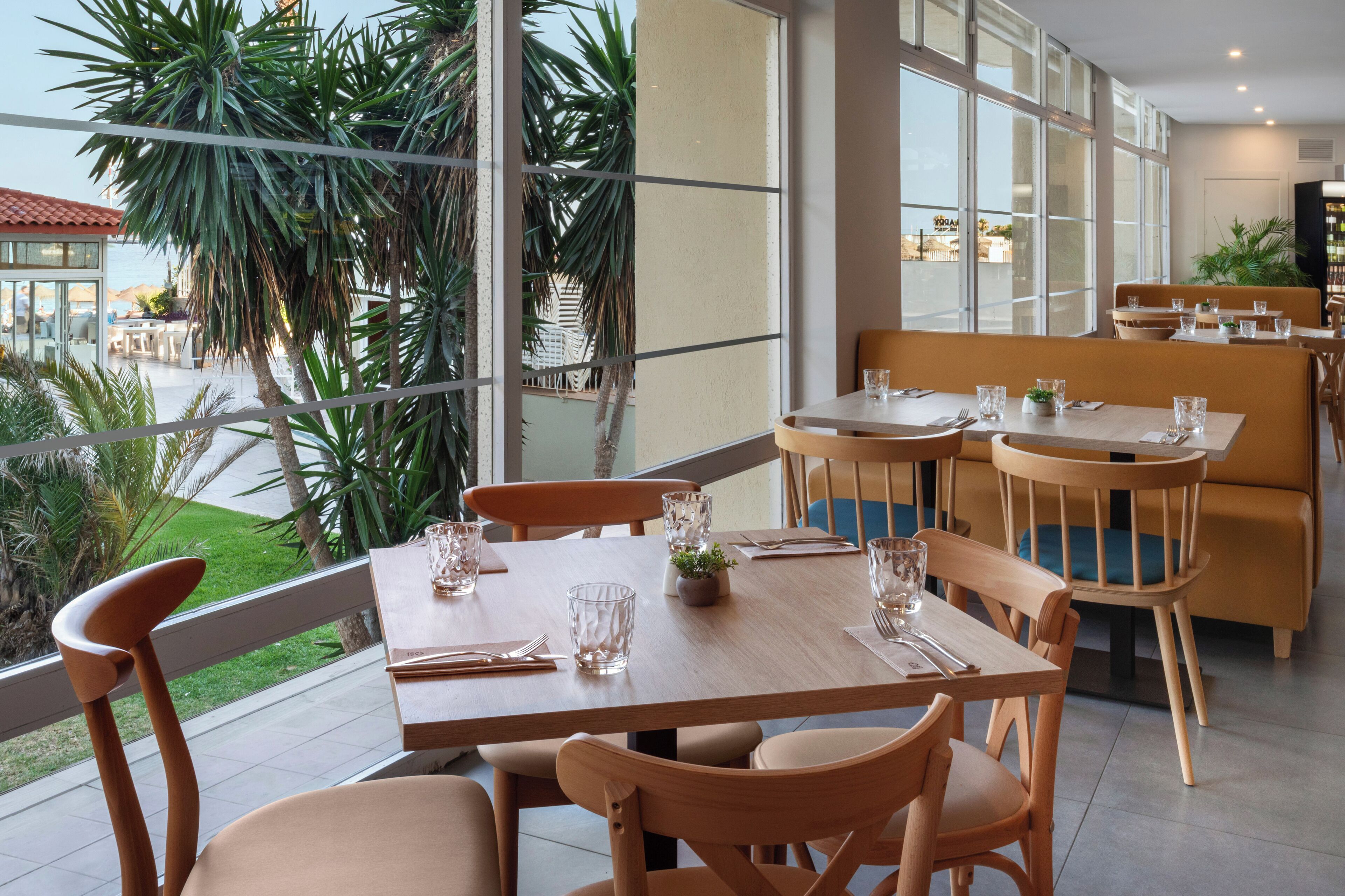 A restaurant with outdoor seating, large windows, and a view of palm trees.