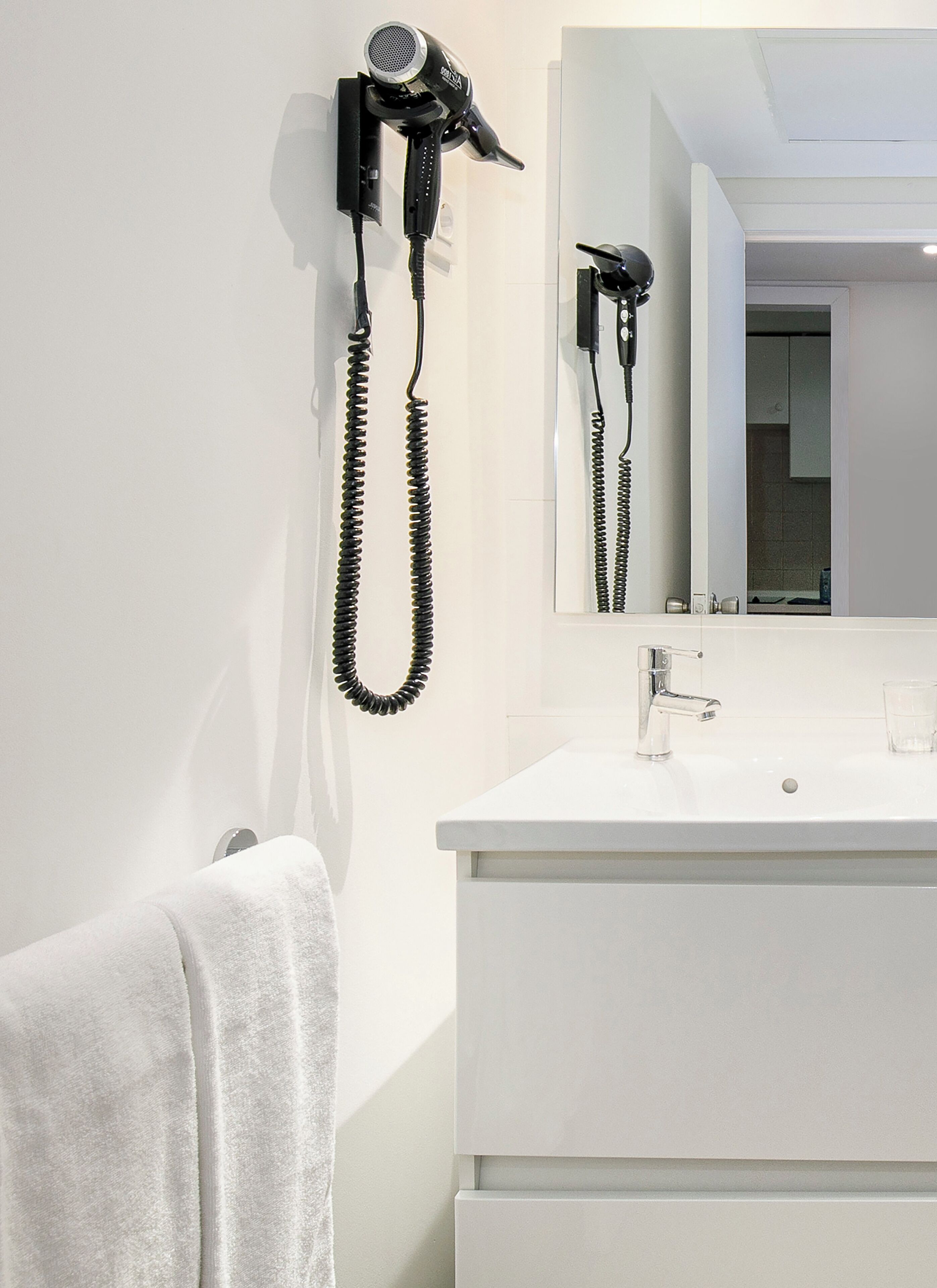 Un baño con lavamanos blanco, un espejo y un secador de pelo montado en la pared.