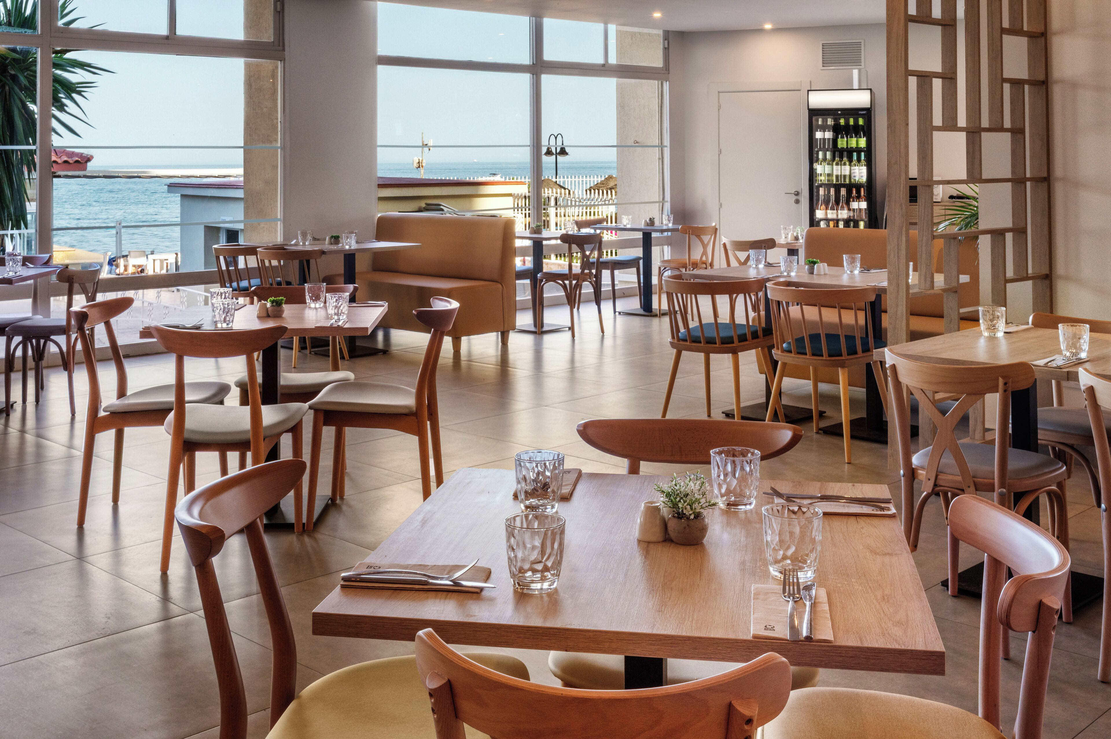 Een restaurant met tafels en stoelen, uitzicht op zee en een bar met flessen.