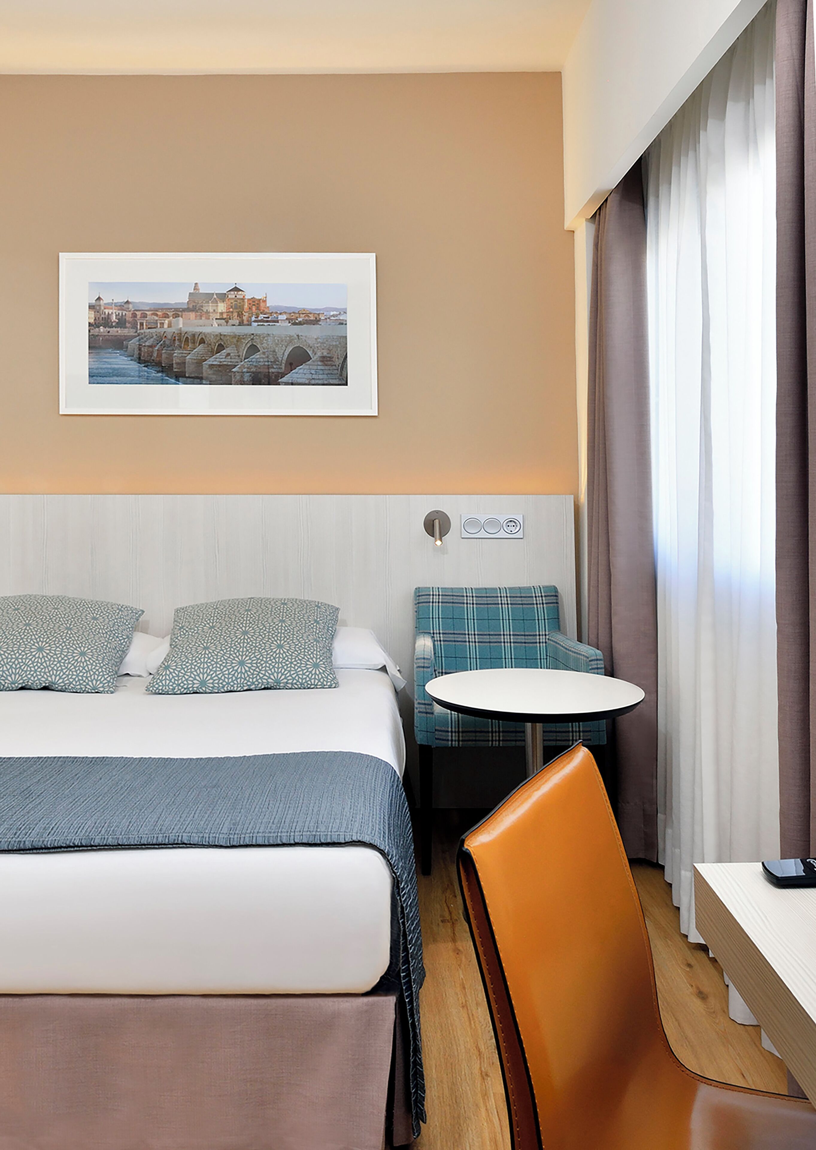 A hotel room with a bed, a seating area with a table, a chair, and a wall-mounted power outlet.