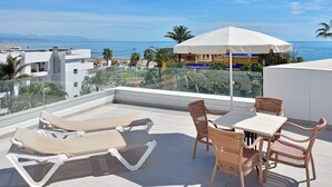 Eine Dachterrasse mit Liegestühlen, einem Tisch und einem Sonnenschirm.