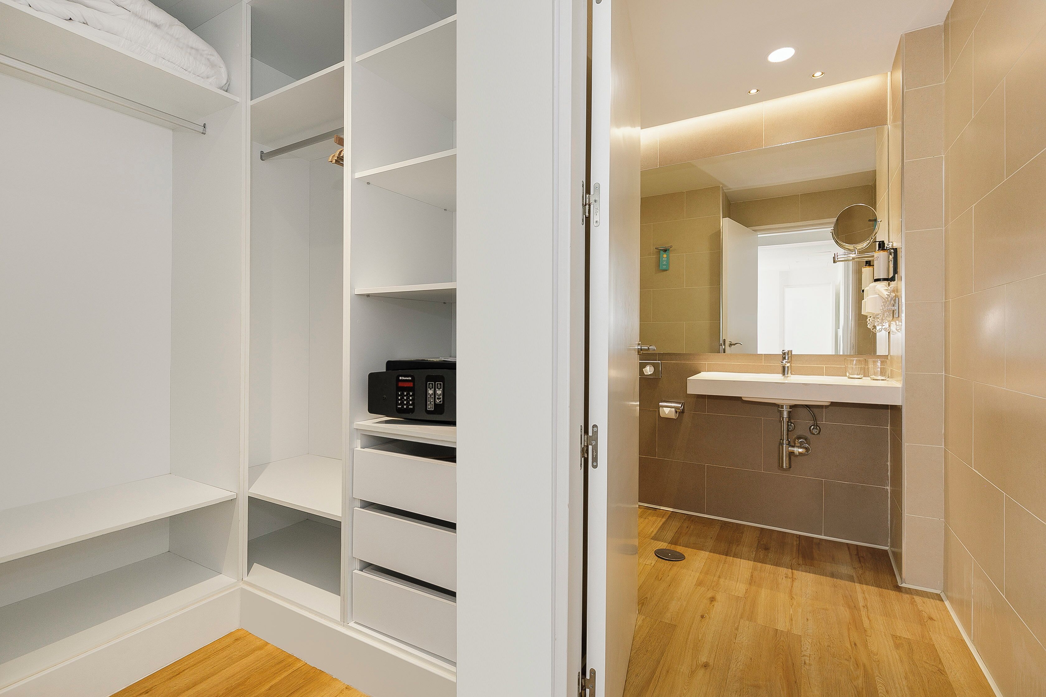Een moderne badkamer met een grote spiegel, een wastafel en een toilet. Er is een wit meubelstuk met lades en planken.