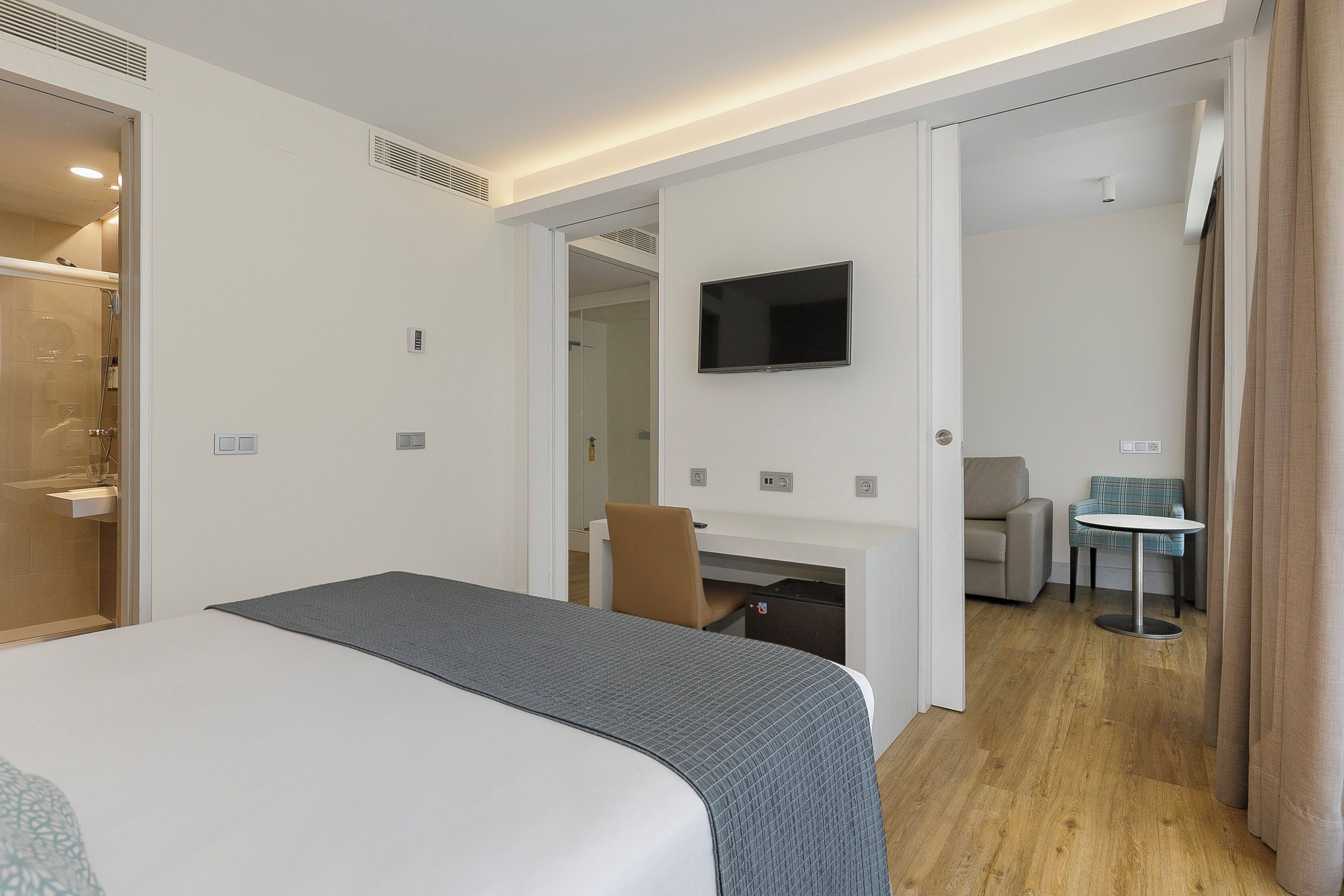 Ein Hotelzimmer mit einem Bett, einem Schreibtisch, einem Sessel, einem Fernseher und einem kleinen Tisch.