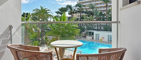 Un balcon avec une piscine, des meubles en osier et une vue sur un bâtiment d’hôtel.