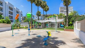 Ein Spielplatz mit verschiedenen Spielgeräten, umgeben von Palmen und Gebäuden.