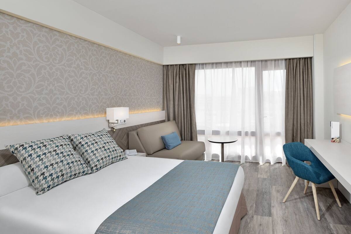 Een hotelkamer met een bed, bureau, stoel, televisie en een raam met gordijnen.