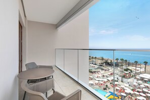 Un balcón con mesa y sillas, con vistas a una zona de resort con piscinas y sombrillas.