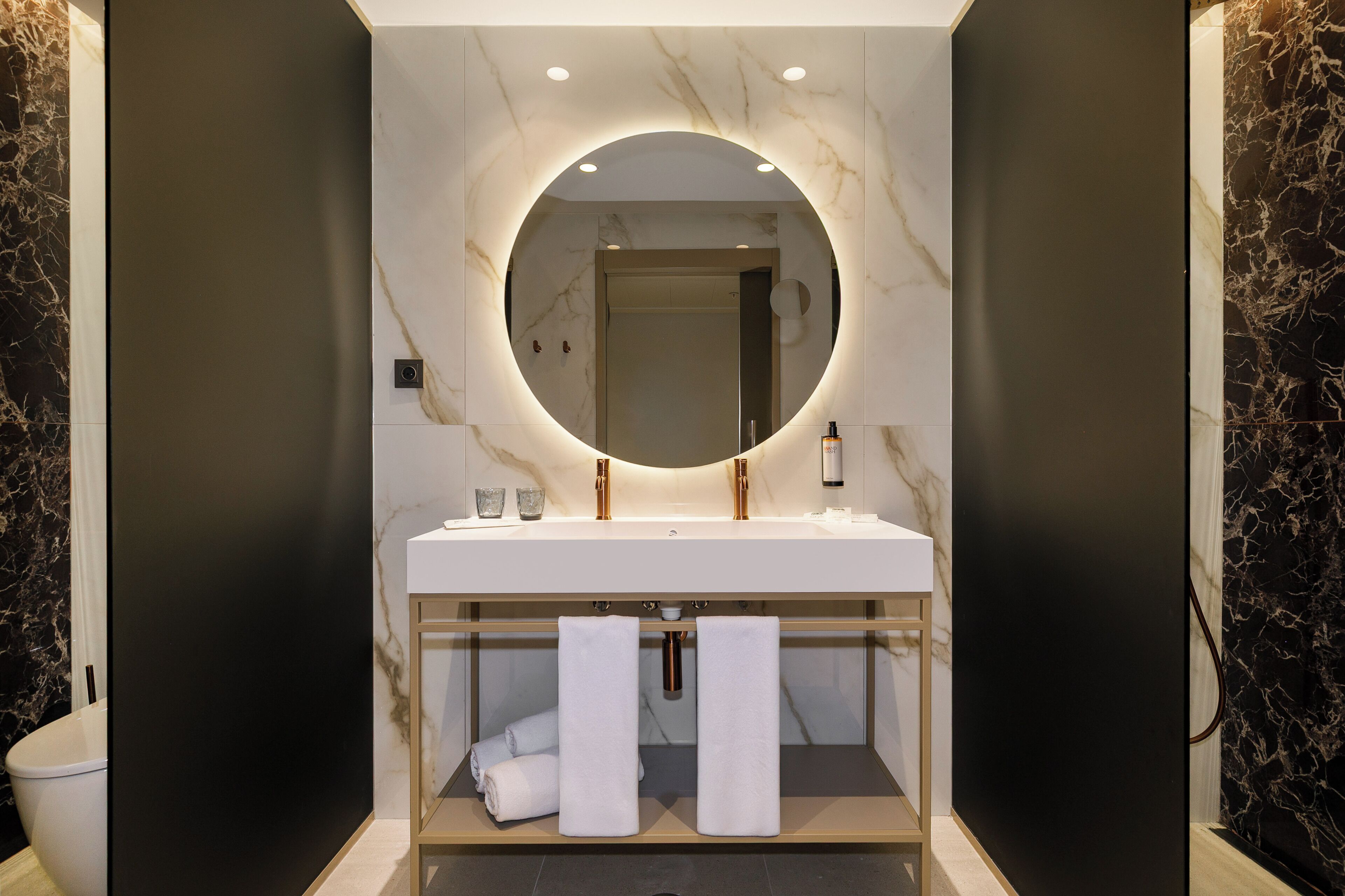 Un baño moderno con tocador de mármol, un espejo redondo y dos toallas.
