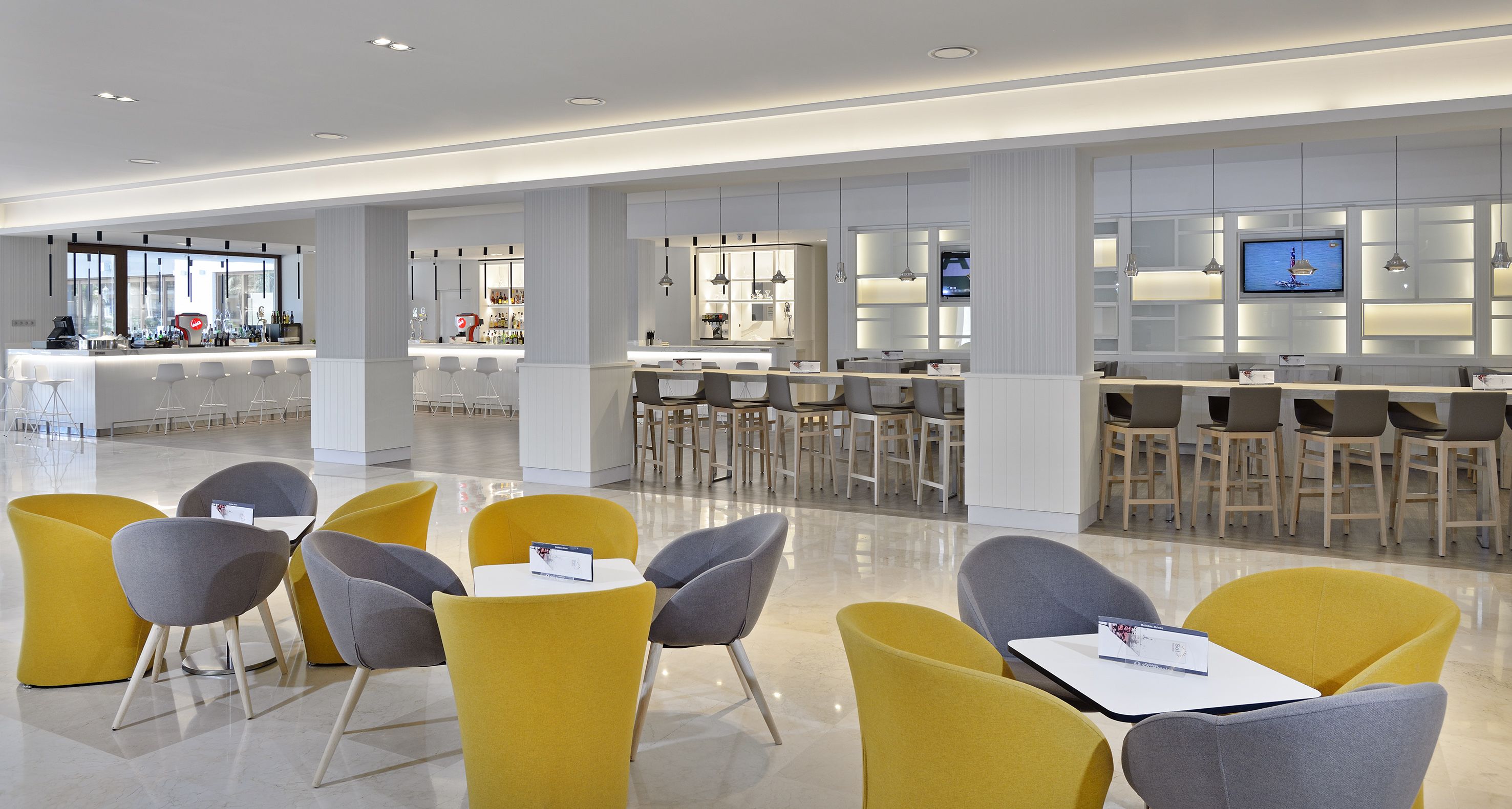 Un hall d’hôtel moderne doté d’un bar, de différents espaces de détente et d’un écran de télévision.