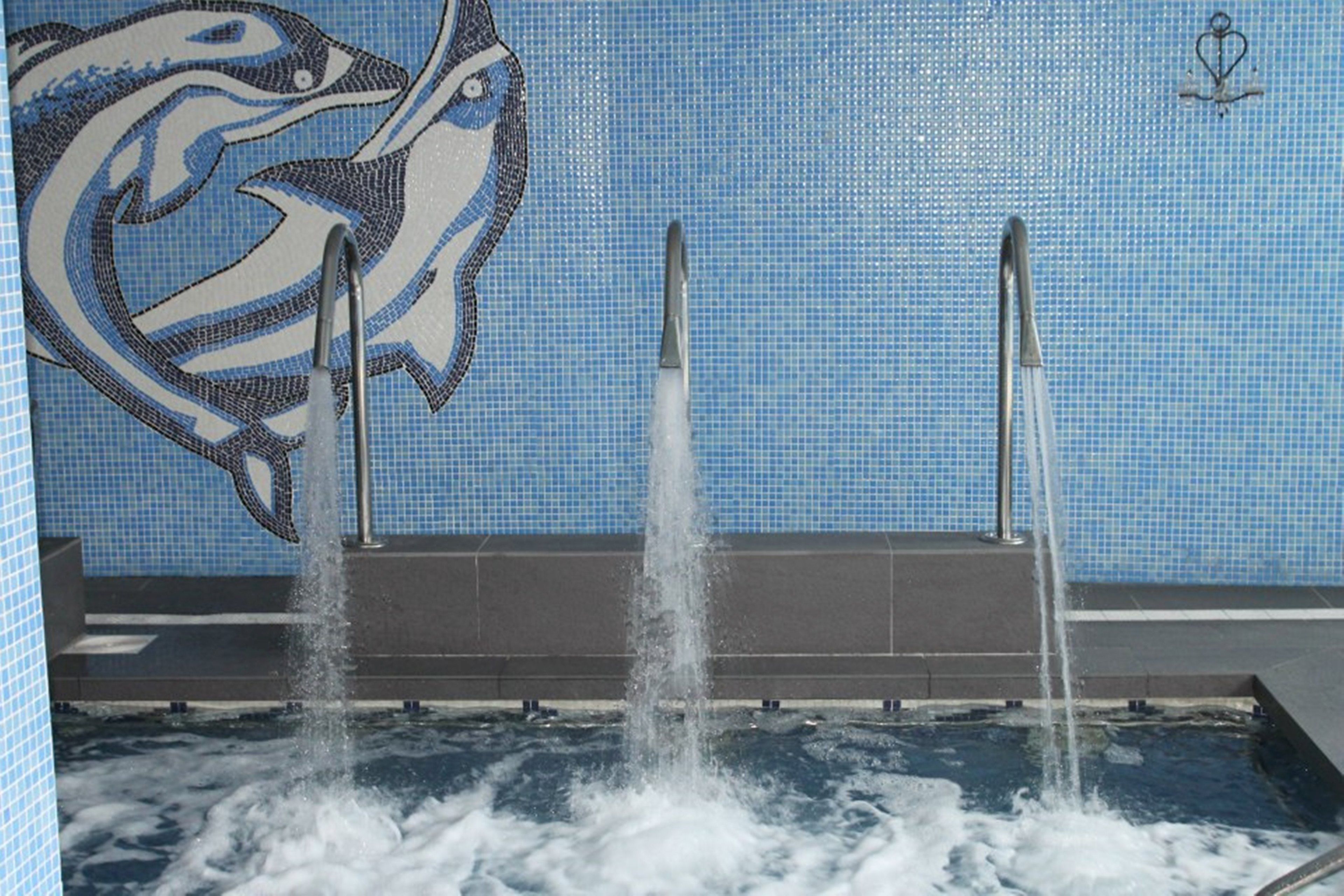 Una piscina con un mural de delfines y tres chorros de agua.