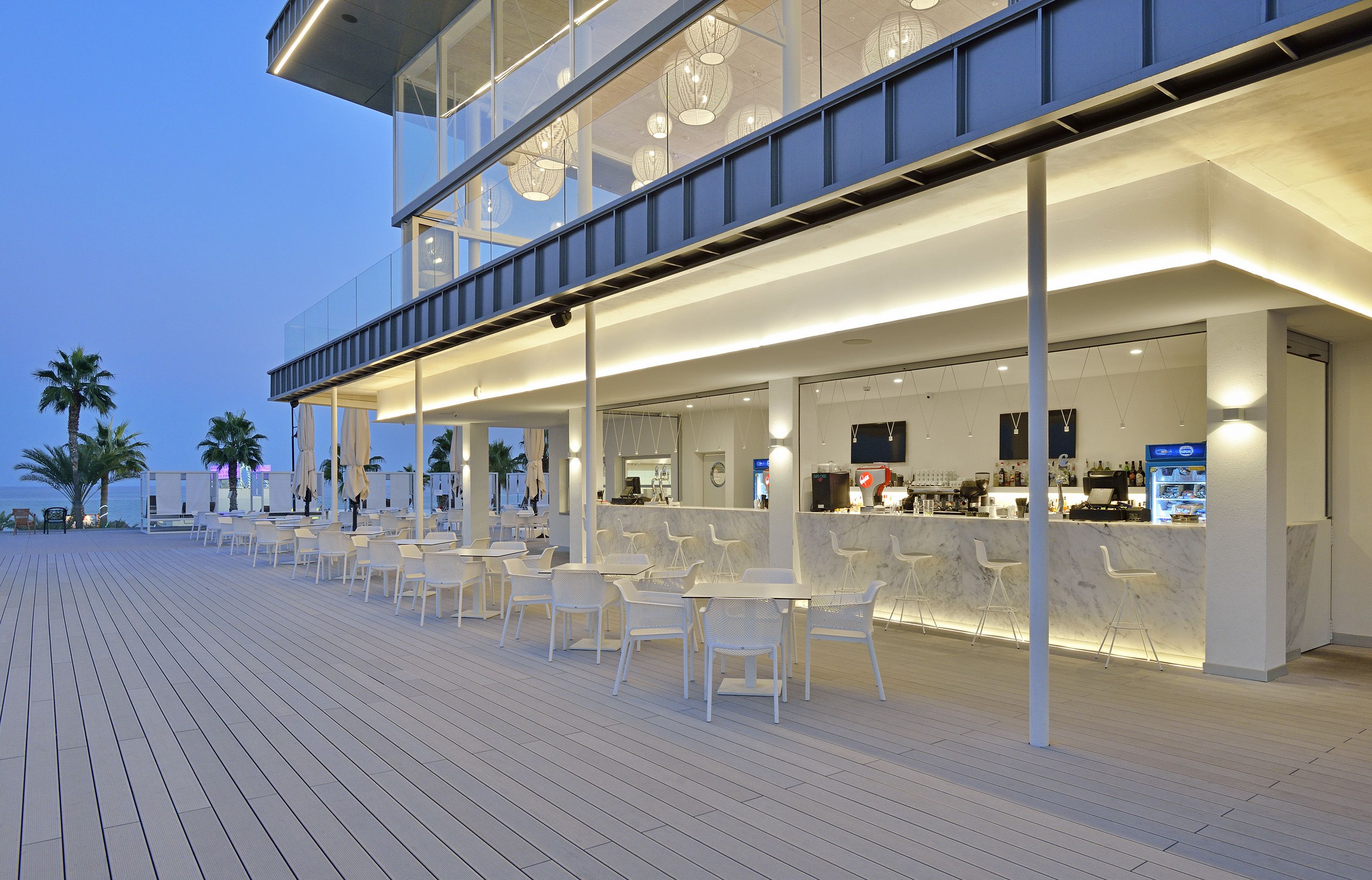 Un espace bar extérieur moderne, doté de sièges et d’un comptoir, offrant une vue sur une étendue d’eau.