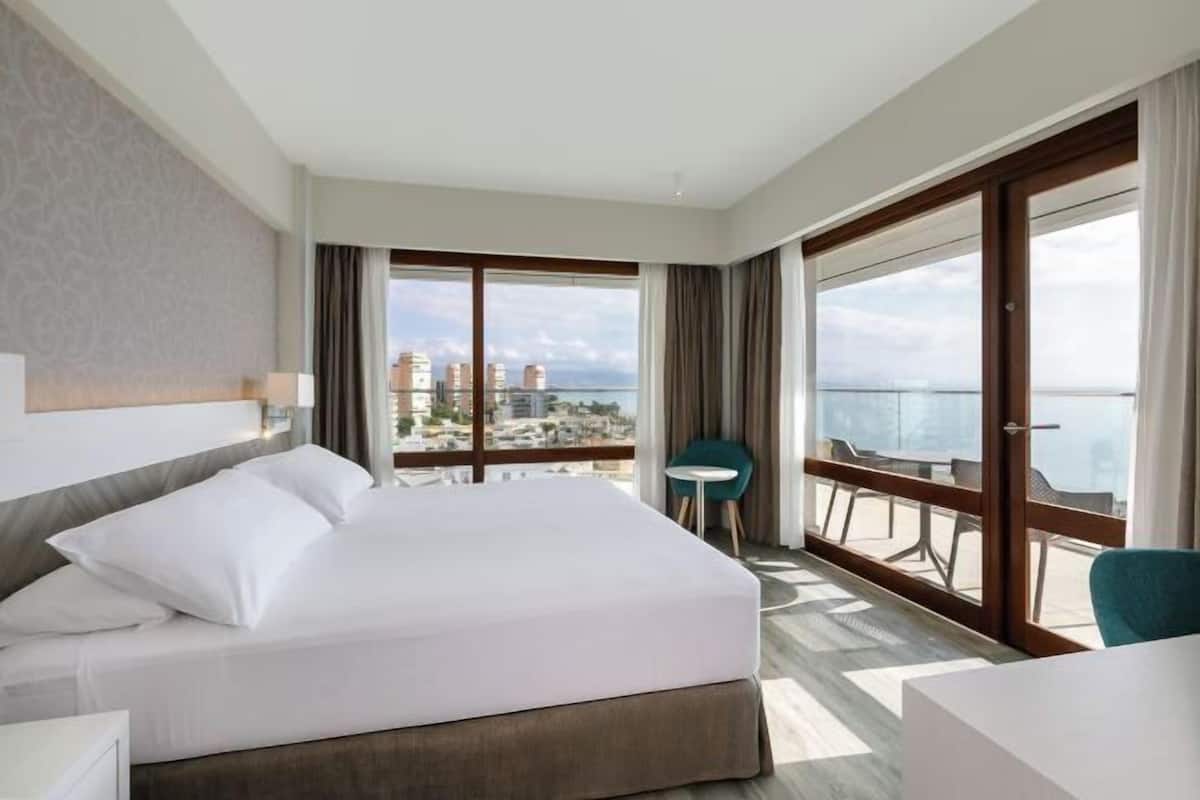 A hotel room with a large bed, a view of the city, and a balcony with outdoor seating.