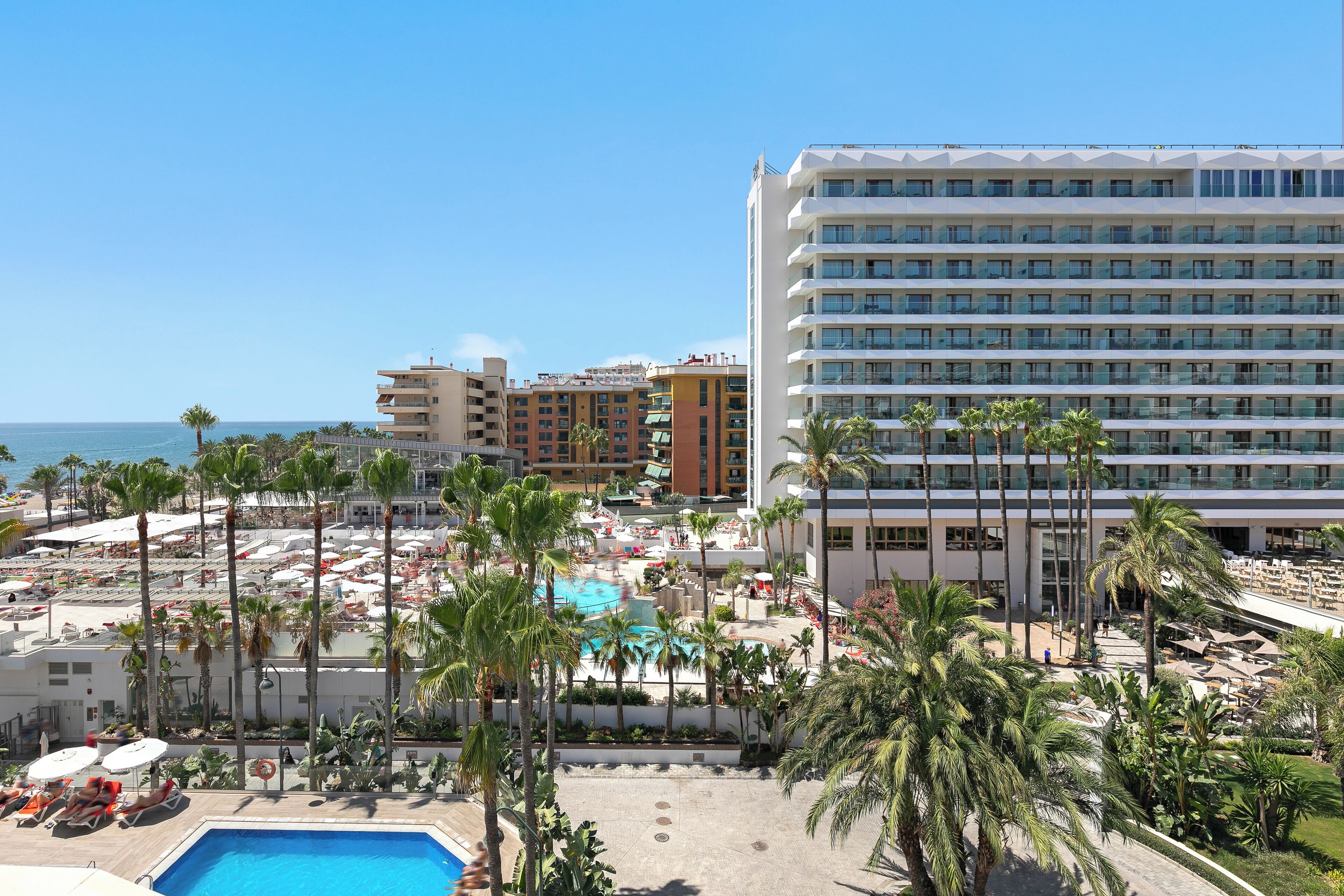 Un hôtel doté d’une piscine, de palmiers et offrant une vue sur l’océan.
